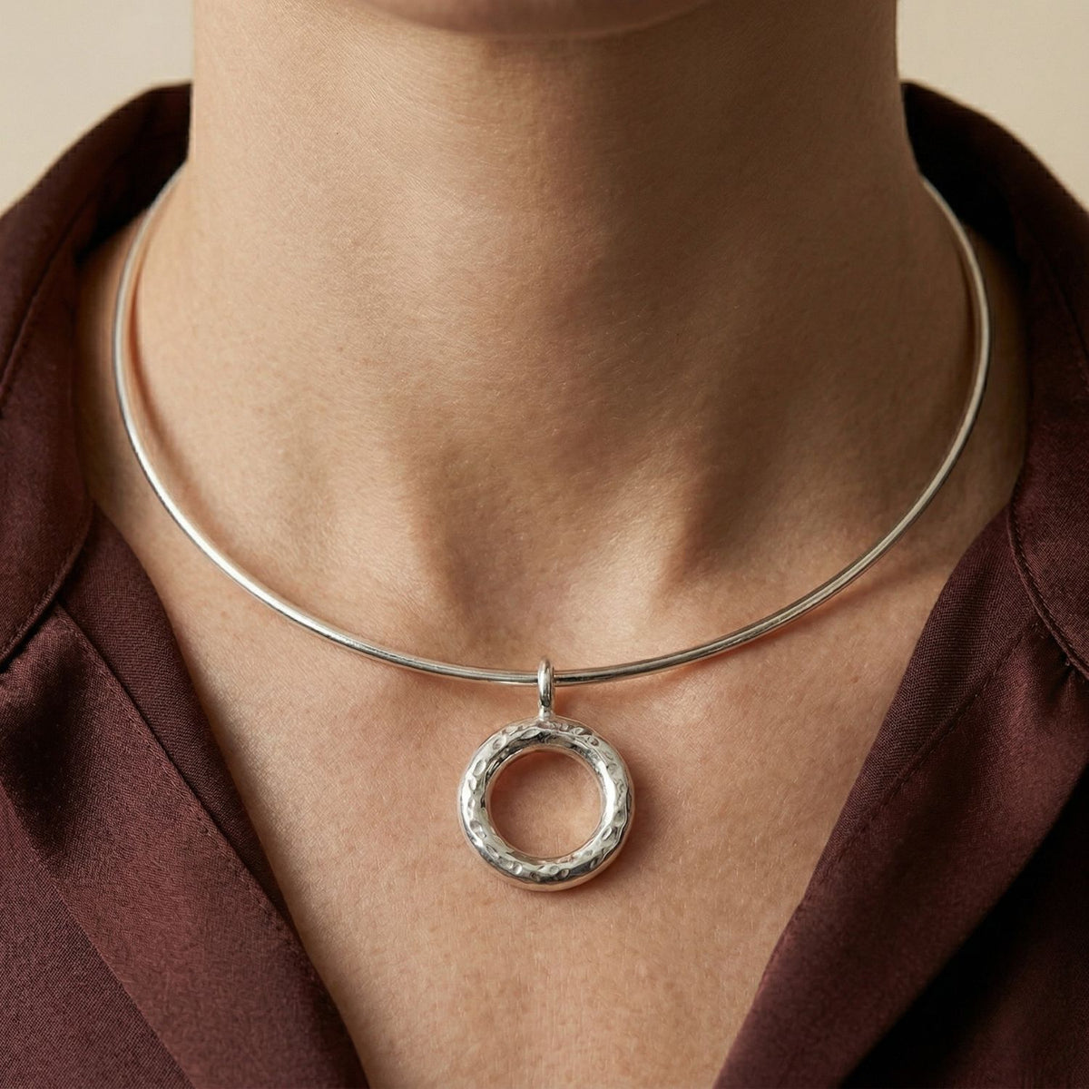 Hand-assembled in our West Hollywood studio, a textured silver doughnut pendant punctuates the collarbone, set against a burgundy shirt and soft beige backdrop. Crafted in small batches using eco-conscious methods. Style Note: effortless from classic shirting to after-dark layers.