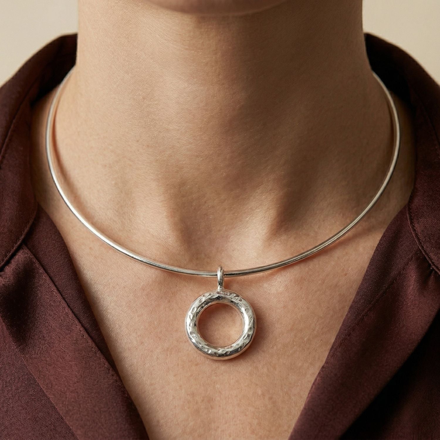 The Silver Doughnut Pendant Collar Necklace by JAREDJAMIN Jewelry Online is a minimalist, modern silver choker with an adjustable lobster clasp and a central textured doughnut pendant in a shiny finish.