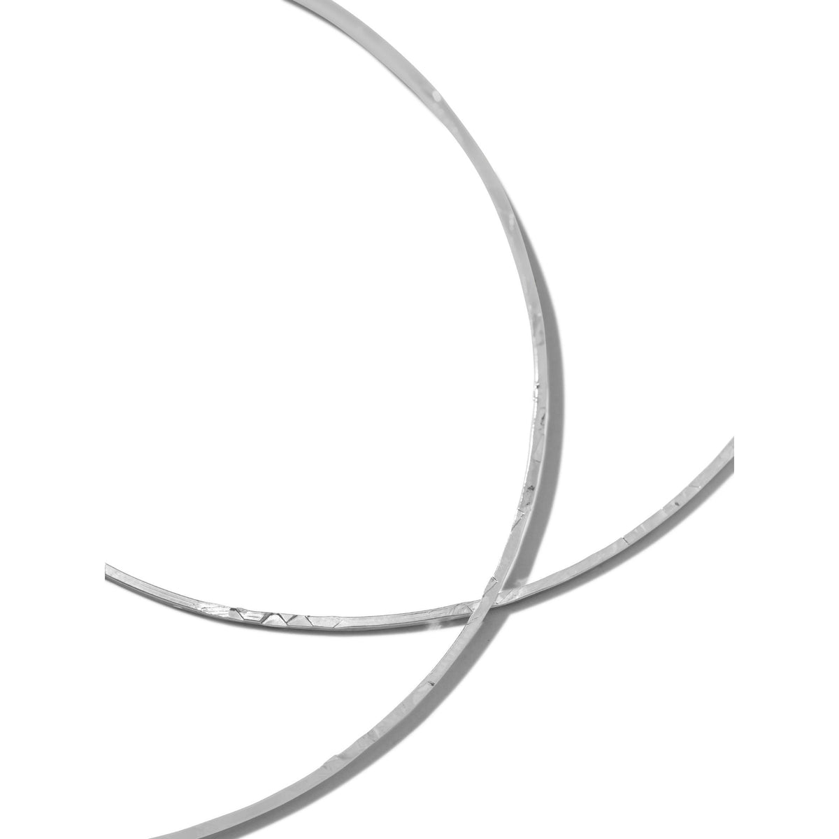 The Silver Halo Textured Hoop Earrings by JAREDJAMIN Jewelry Online feature two rhodium-plated brass hoops in metallic silver, intersecting with subtle texture and reflections against a plain white background for a minimal, modern look.