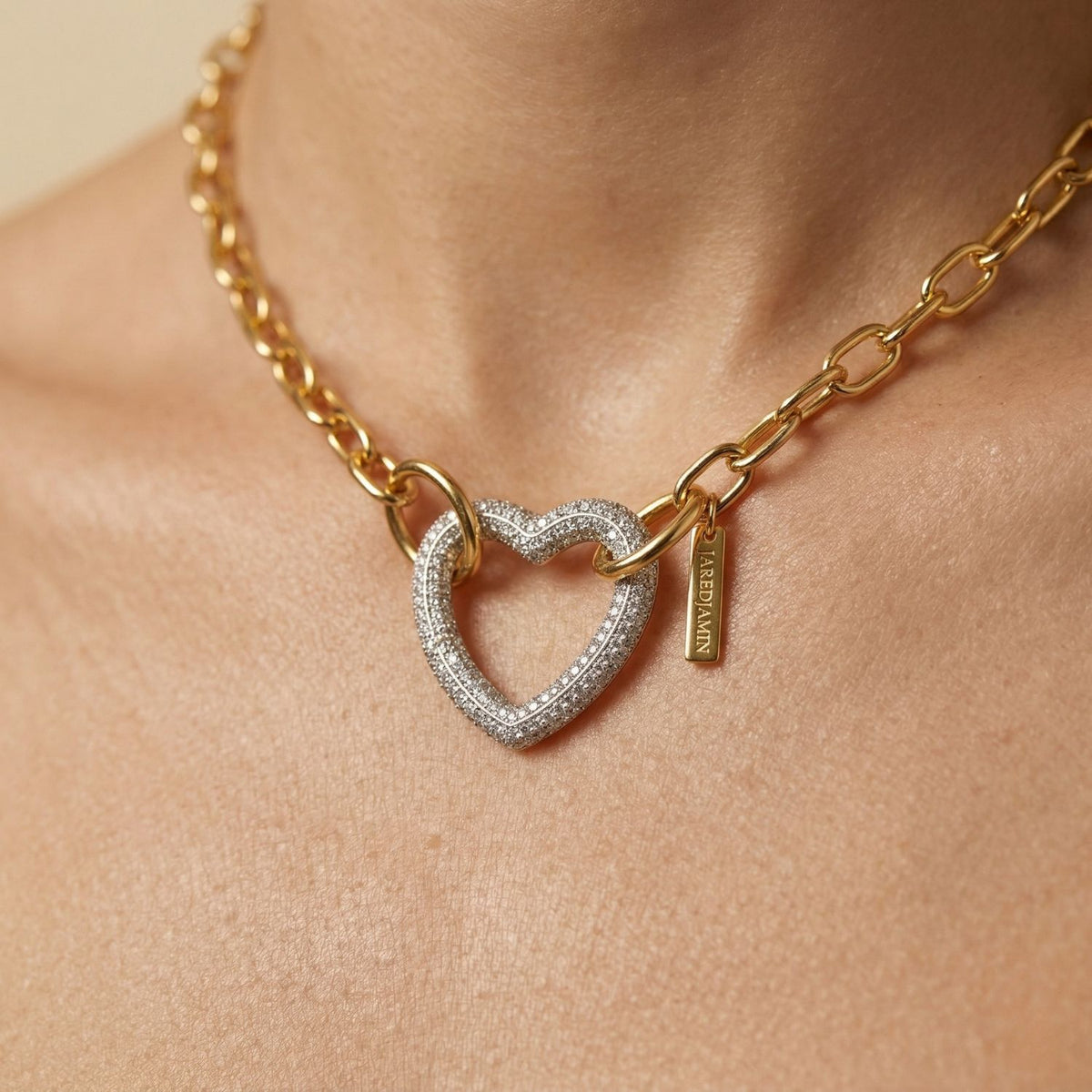 A close-up of our hand-assembled Silver Heart Pavé Clicker Clasp necklace—cubic zirconia heart refracts light, anchored by a branded tag—crafted in small batches at our West Hollywood studio. Style Note: sharp with suiting or layered after-hours.