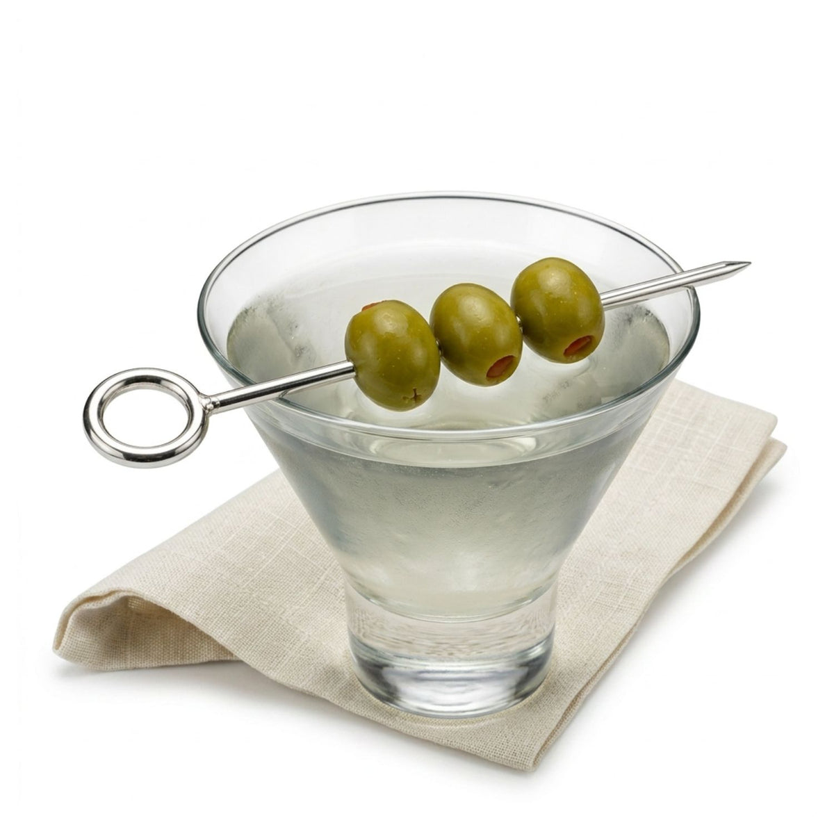 Luxury mixology styling shot of a crystal martini glass holding a clear cocktail, with the 6 5/8-inch Silver It's Five o' Clock Cocktail Skewer resting across the rim, beautifully skewering three green gourmet olives to demonstrate its length, weight, and elegant function.