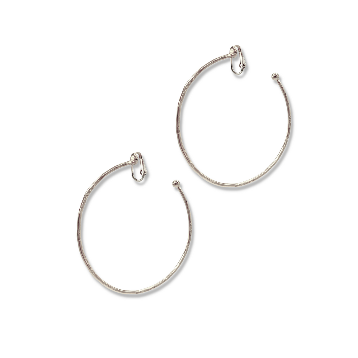 Les argent Medium Hooptastic Clip On créole boucles d'oreilles par JAREDJAMIN Bijoux en Ligne présentent large, thin argent créoles avec a hammered texture, small ball detail, white rhodium finish, et hinged clasp, displayed against a fond blanc.