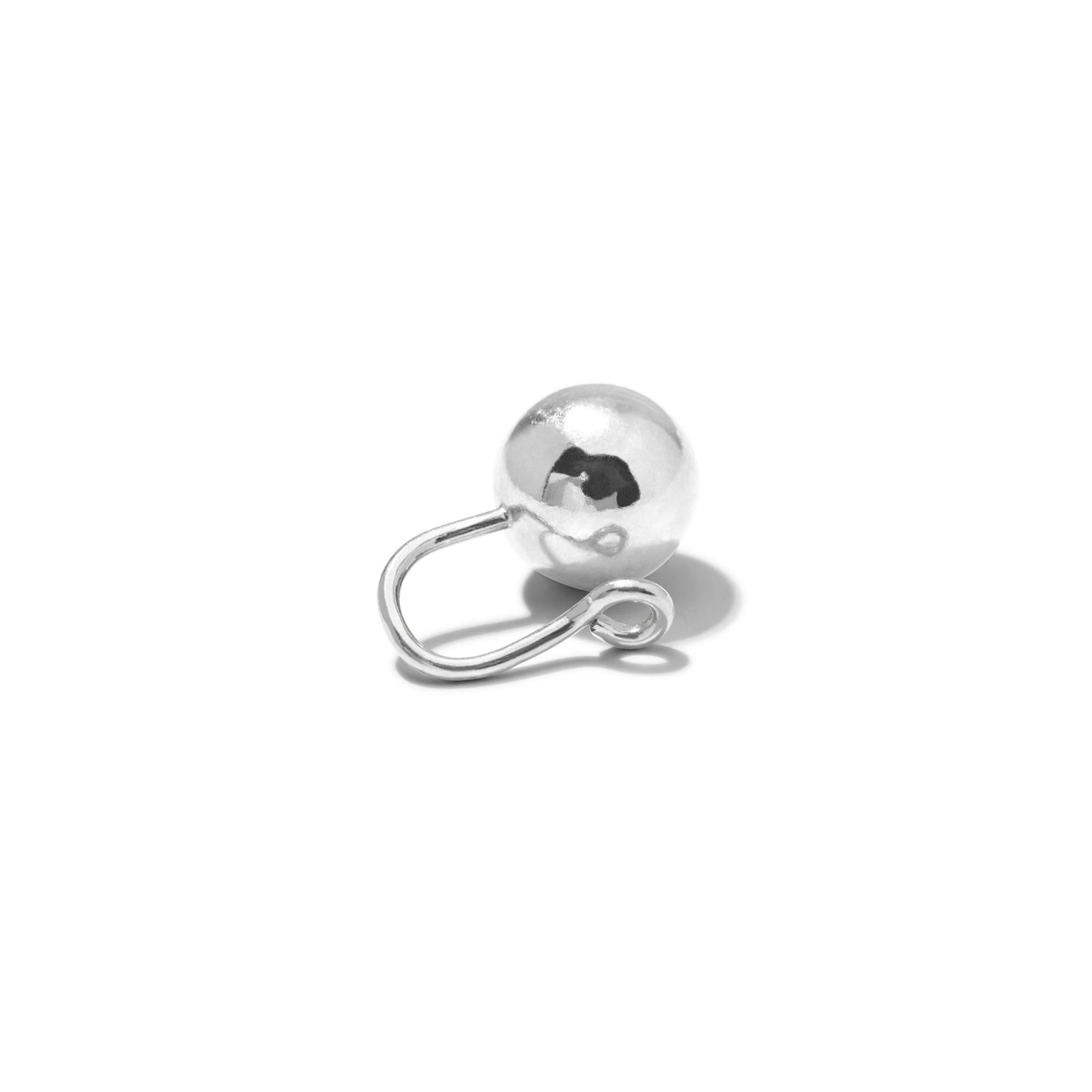 The Silver Orbita Ear Cuff Earring by JAREDJAMIN Jewelry Online, featuring a shiny, spherical design with a smooth surface and curved latch-back closure, rests on a white background casting a soft gray shadow to the right.