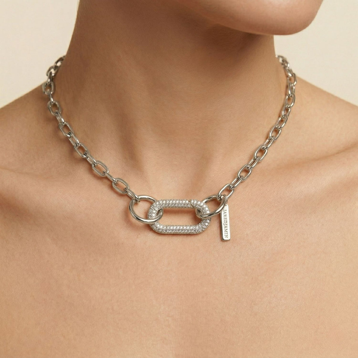 A close-up captures a neck draped in our hand-assembled, West Hollywood–forged Silver Oval Pavé Clicker Clasp: a weighty, eco-conscious chain punctuated by pavé ovals and signature tag. Style note: refines both suiting and evening slip dresses with ease.