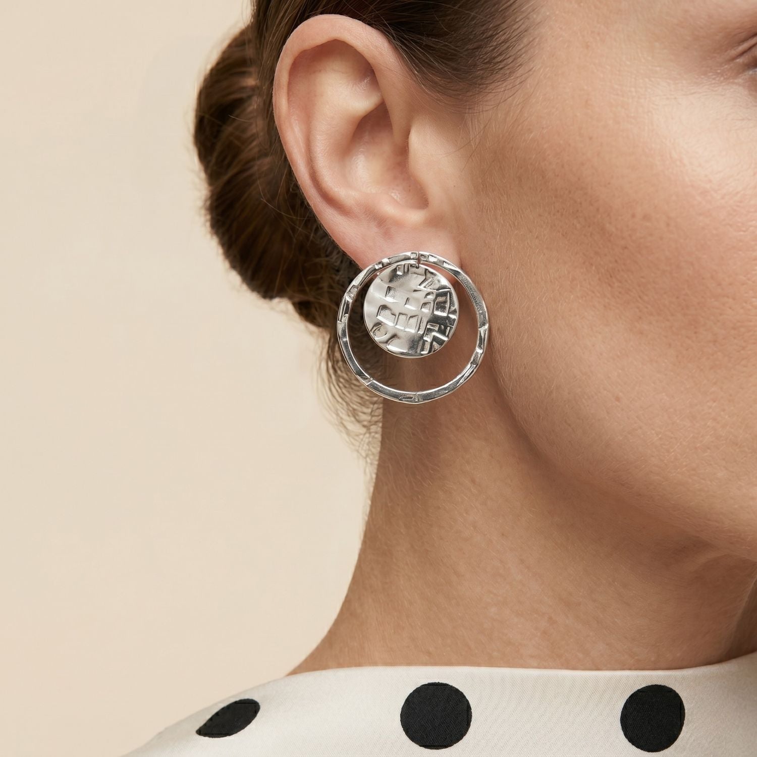 Two Silver Peacock Eye Clip On Earrings by JAREDJAMIN Jewelry Online are displayed on a white background, each featuring a round textured disk with a hammered grid pattern and an irregular hoop for a handcrafted look.