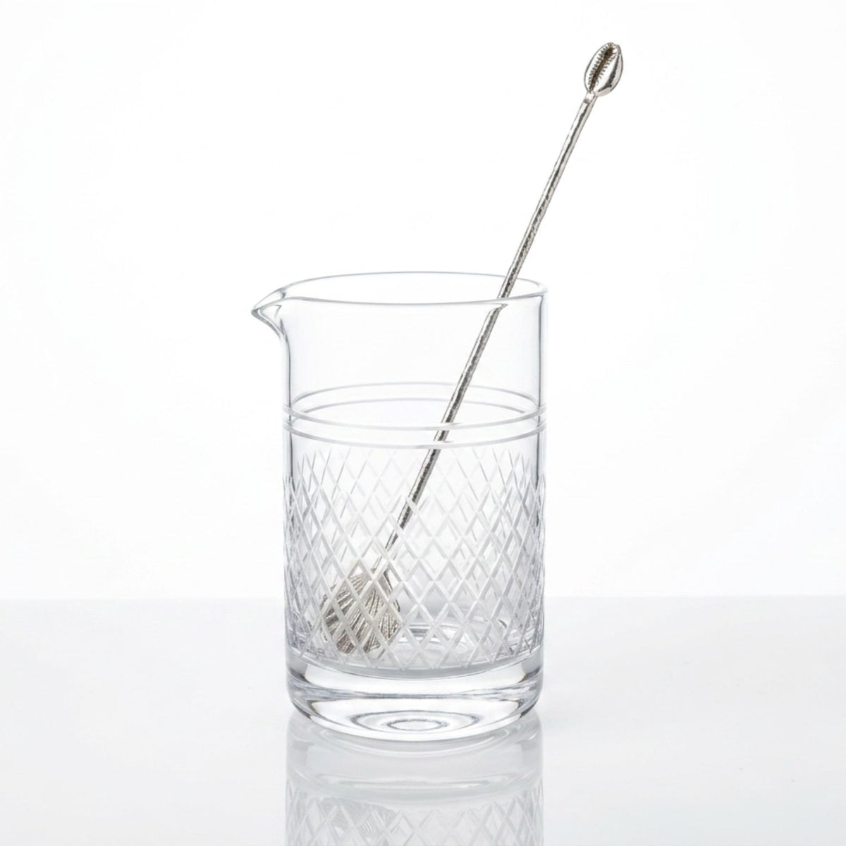 Elegant bar styling view of the handcrafted silver cocktail stirrer resting inside a classic, crisscross cut-crystal cocktail mixing pitcher, illustrating its 9.25-inch proportion and coastal luxury lifestyle aesthetic.