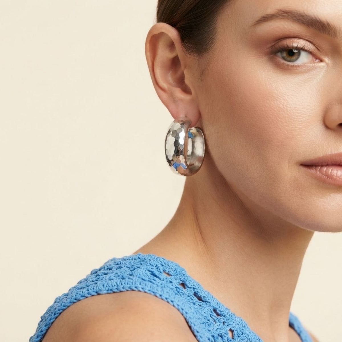 Side view profile of a model wearing the 1.25-inch silver Sabine Wide Hoop Earring, illustrating its architectural scale and reflective finish styled alongside a blue crochet top.