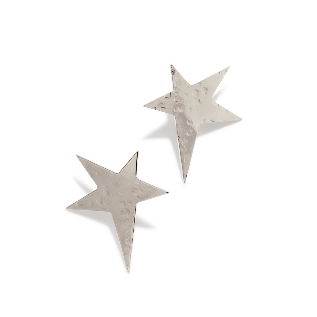 Los JAREDJAMIN Joyería Online plata Shooting Star pendiente de botón Post pendientes presentan metallic, hammered plata star shapes con five uneven arms, shown diagonally sobre un fondo blanco reflecting light y casting subtle shadows.