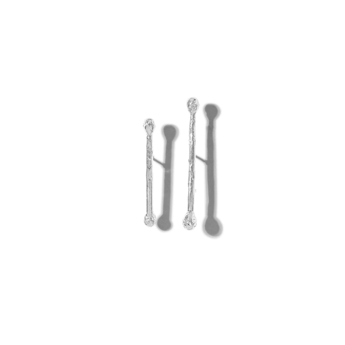 Un minimal image displays JAREDJAMIN Joyería Online's plata Stix Post pendientes: three vertical rods of different lengths, con rounded ends y Platinum-to-plata Plating, evenly spaced sobre un fondo blanco con soft gray shadows.