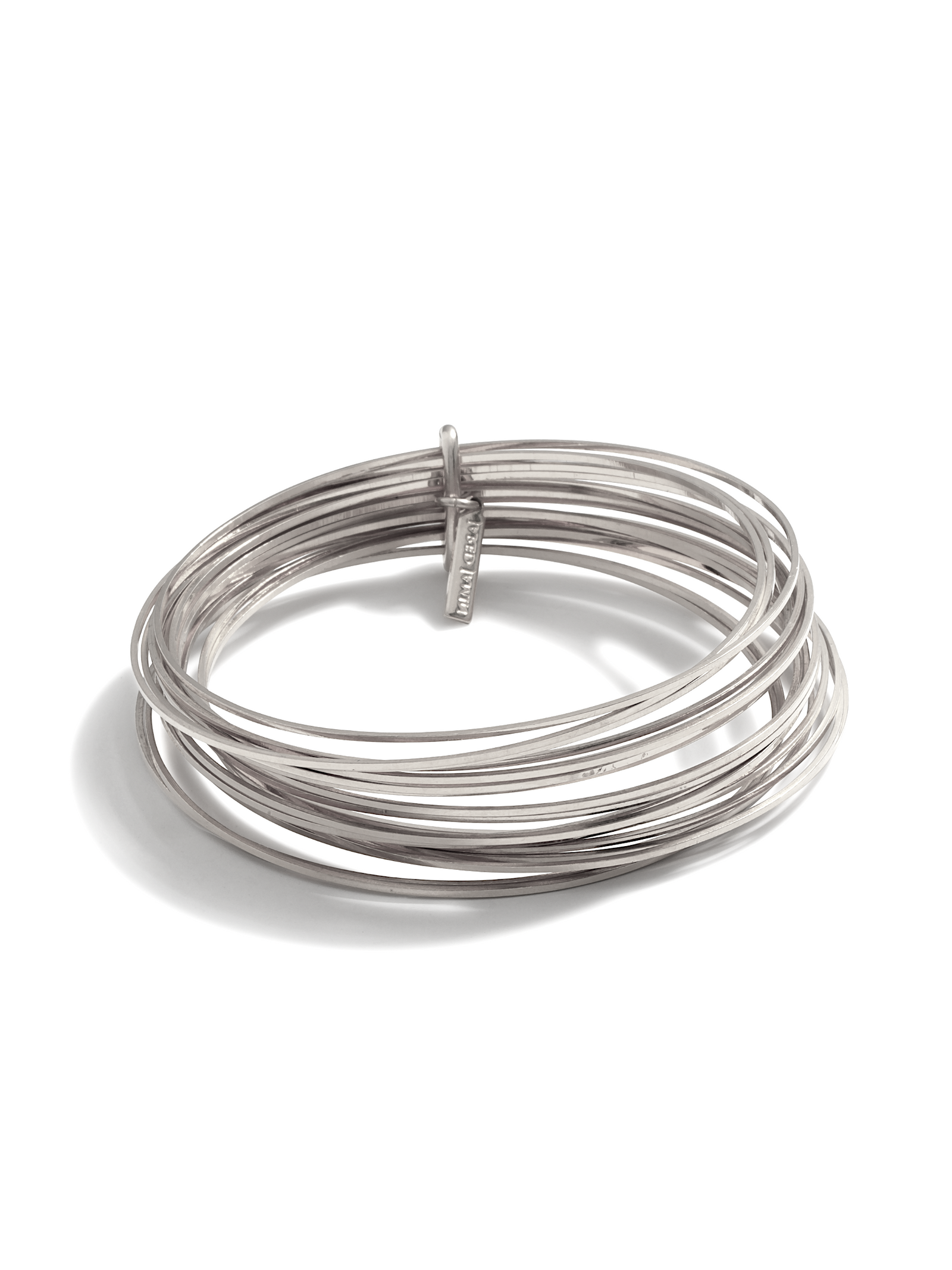 The Silver Twenty Something Bangle Stack from JAREDJAMIN Jewelry Online features seven slim, silver-plated bangles interlocked by a rectangular bar engraved with the brand name, all with a smooth, polished finish.
