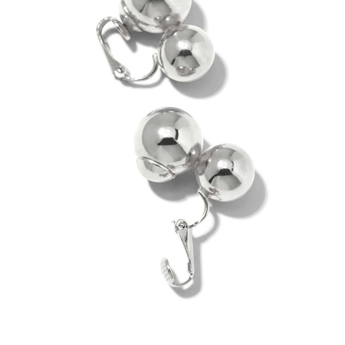primer plano of JAREDJAMIN Joyería Online’s plata Uptown Orbita Clip On pendientes, each showcasing two connected brillante plata spheres in different sizes con a vintage-inspired non-pierced clip mechanism sobre un fondo blanco.