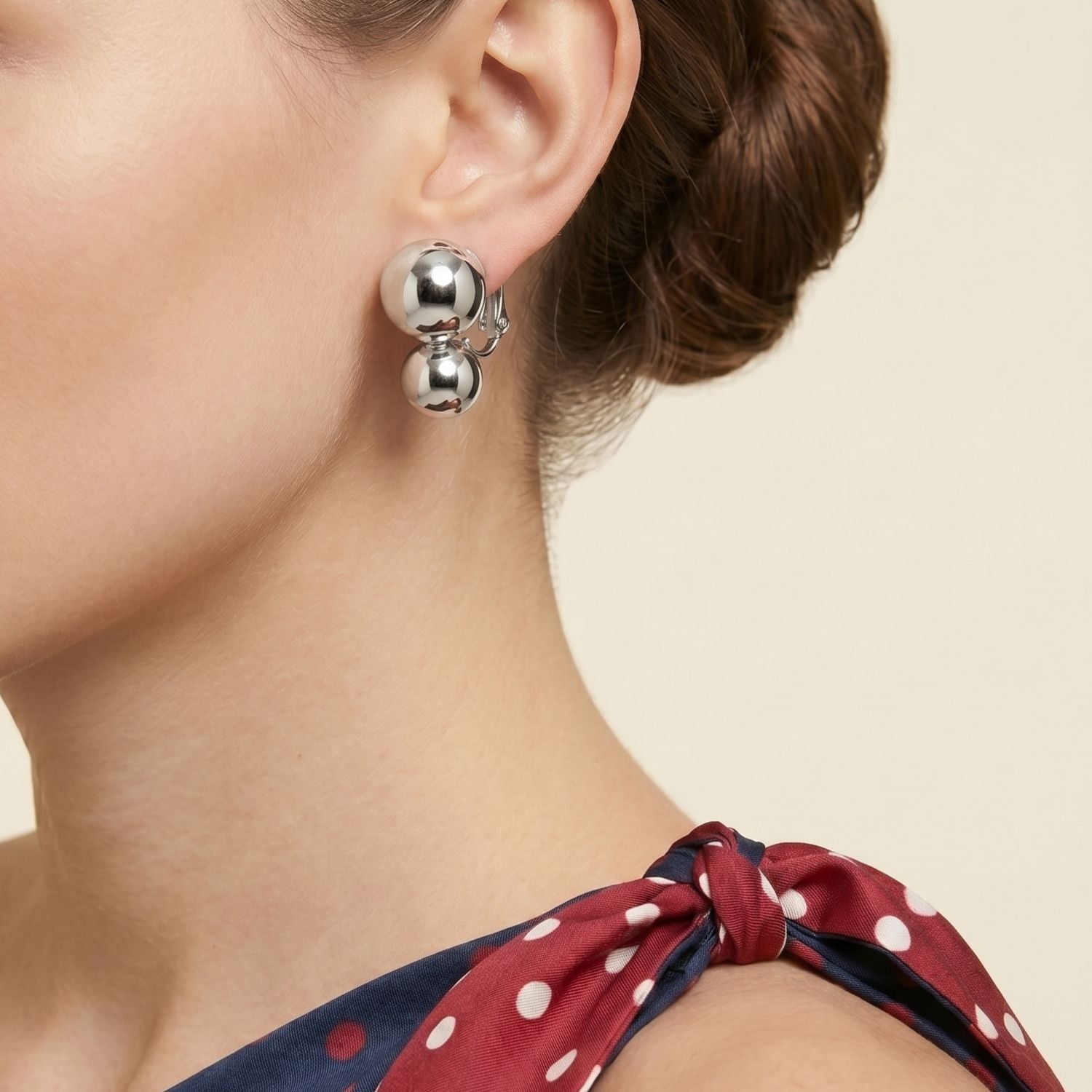 Los plata Uptown Orbita Clip On pendientes de JAREDJAMIN Joyería Online presentan two smooth, reflective plata spheres stacked vertically con a hinged clasp, offering vintage flair. exhibido sobre a plain fondo blanco.