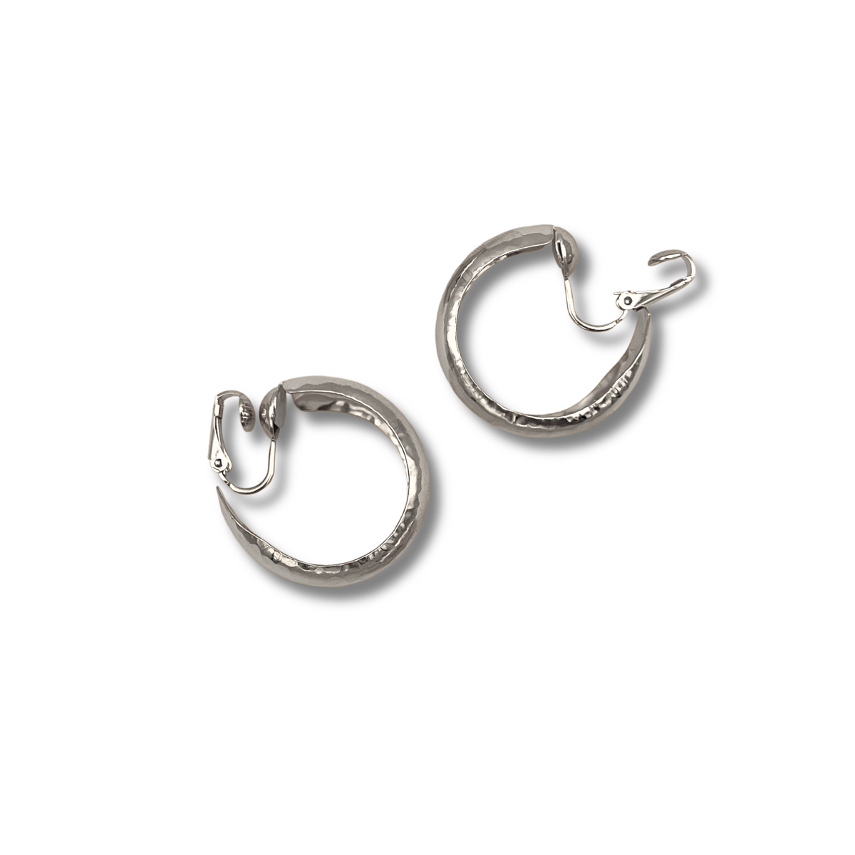 Les argent Rush créole boucles d'oreilles par JAREDJAMIN Bijoux en Ligne présentent argent-plated, texturé créoles avec hinged clip clasps et a hammered finish that reflects light, shown against a fond blanc avec soft gray shadows below each boucle d'oreille.