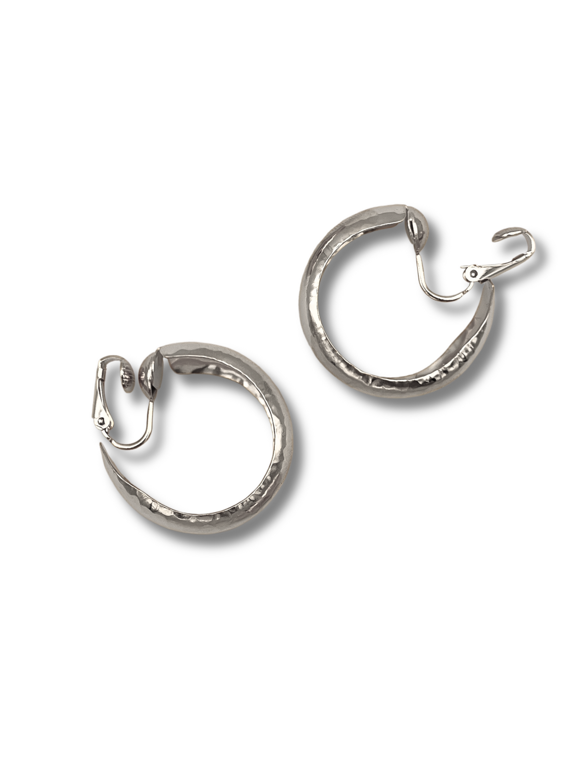 The Silver Rush Hoop Earrings by JAREDJAMIN Jewelry Online feature a secure clasp closure and a textured, hammered finish for a polished yet artisanal look. Positioned diagonally against a white backdrop, they cast soft shadows, adding an elegant touch to girls&#39; jewelry collections.