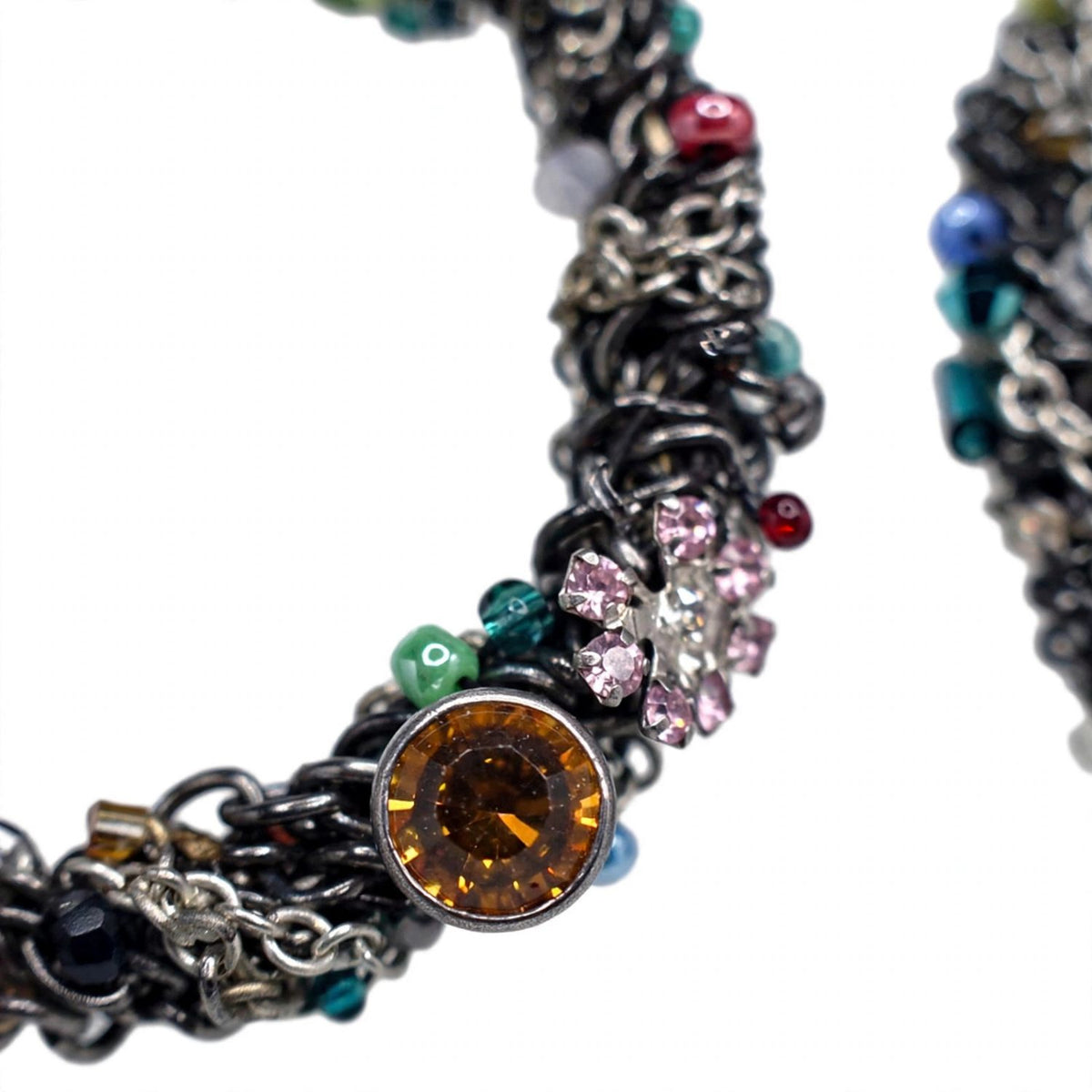 Close-up of a Simone Clip On Earring hoop — dark hand-crocheted wire densely set with crystals, a large amber cabochon, a small pink flower cluster, green and red beads, clear rhinestones and silver-tone chain links, on a white background