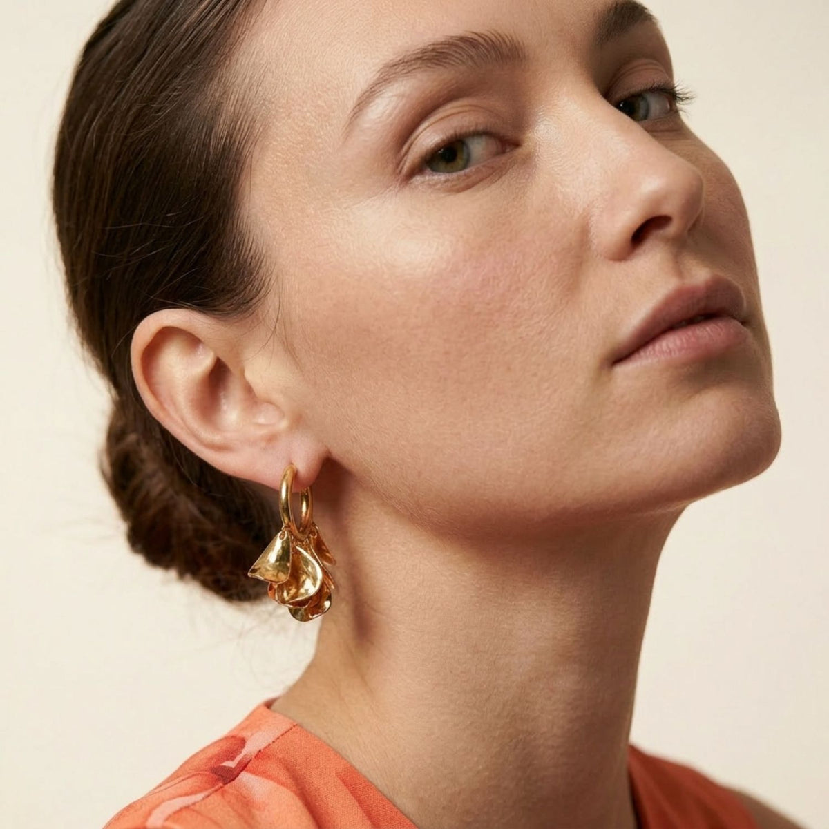 Three-quarter portrait view of a model wearing the gold Petali flower hoop earrings, showcasing their wearable everyday statement scale and how they catch light near the jawline.
