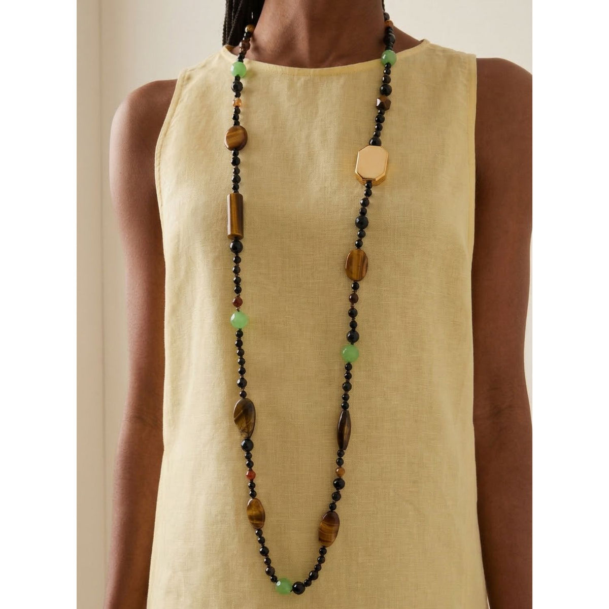 A woman in a sleeveless yellow linen top wears the hand-assembled Sorrento Gemstone Knotted Necklace—Tiger’s Eye and 18k gold-plated beads punctuate the line, crafted small-batch in West Hollywood. Style Note: shifts from tailored shirting to silk after-dark.