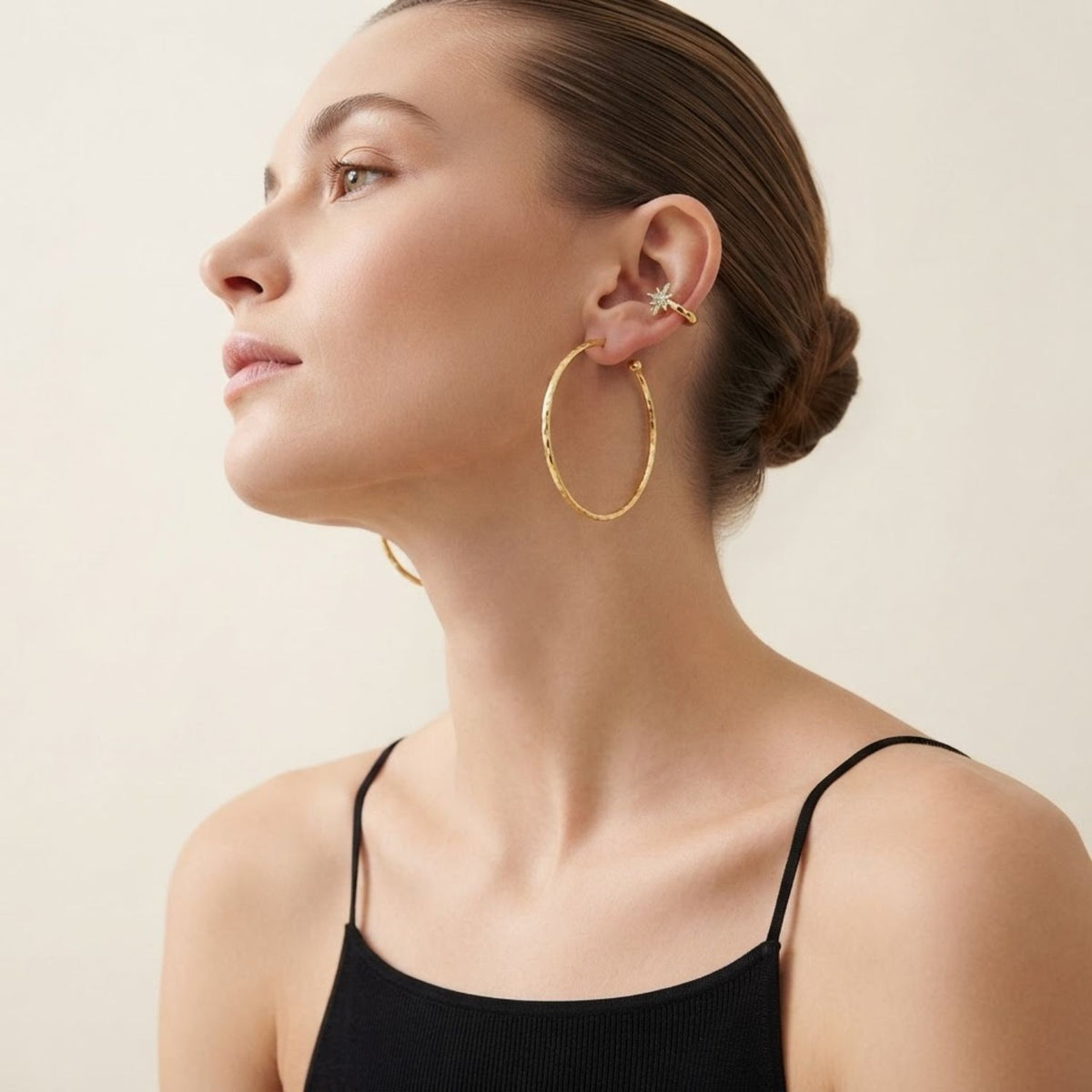 Side view portrait of a model showcasing the Astra Star Ear Cuff styled on the upper cartilage, paired with oversized thin gold hoop earrings for a layered, contemporary look.
