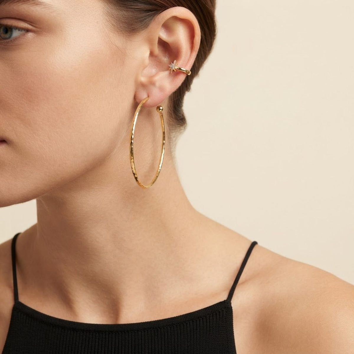 Macro view focusing on a model's ear, demonstrating the comfortable slip-on fit and fine-jewelry sparkle of the gold and clear CZ Astra star cuff alongside a thin gold hoop earring.
