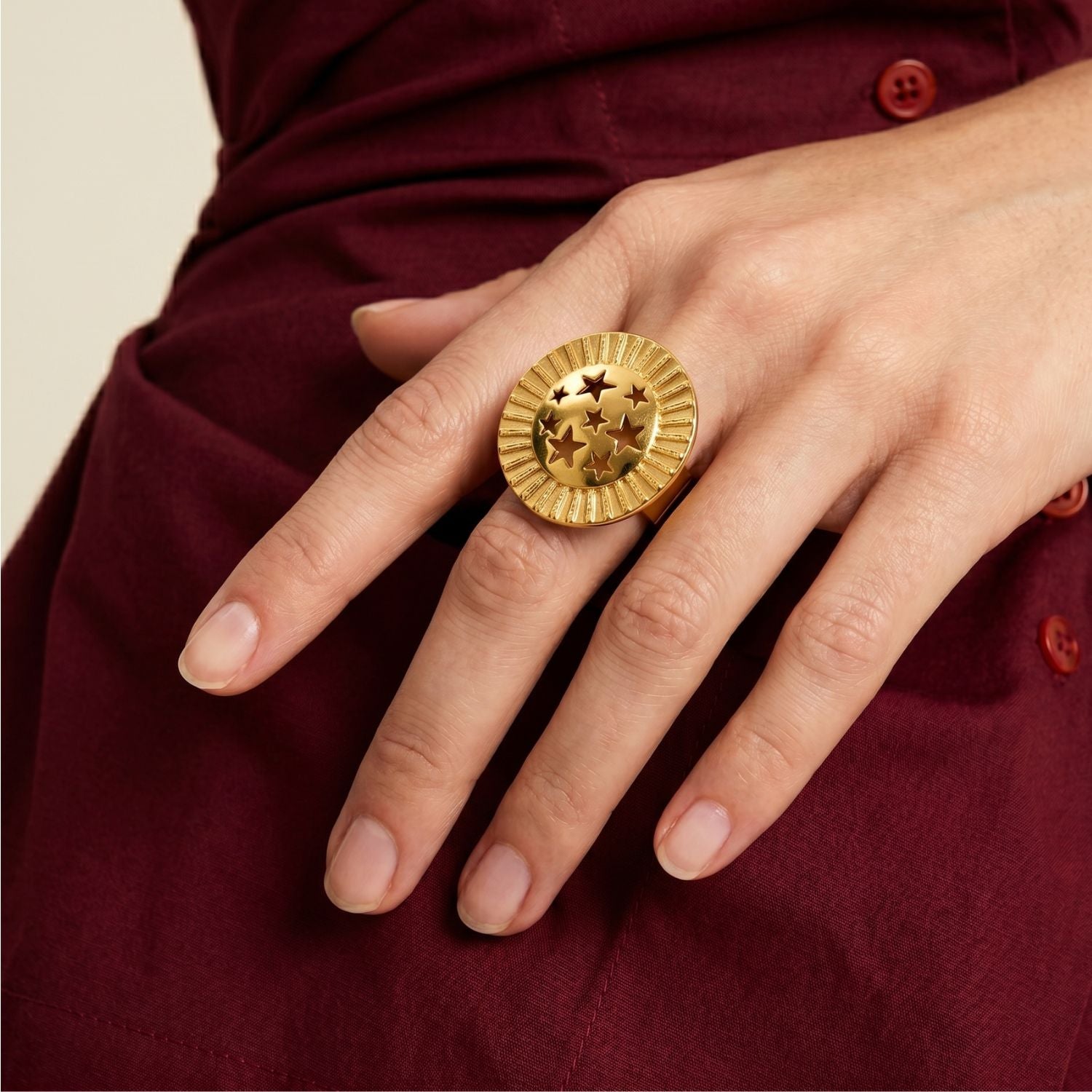 Los Starburst llamativo anillo de JAREDJAMIN Joyería Online showcases five embossed stars on an 18K bañado en oro, round design con a ridged border, capturing celestial elegance. Presented sobre un plain fondo blanco.