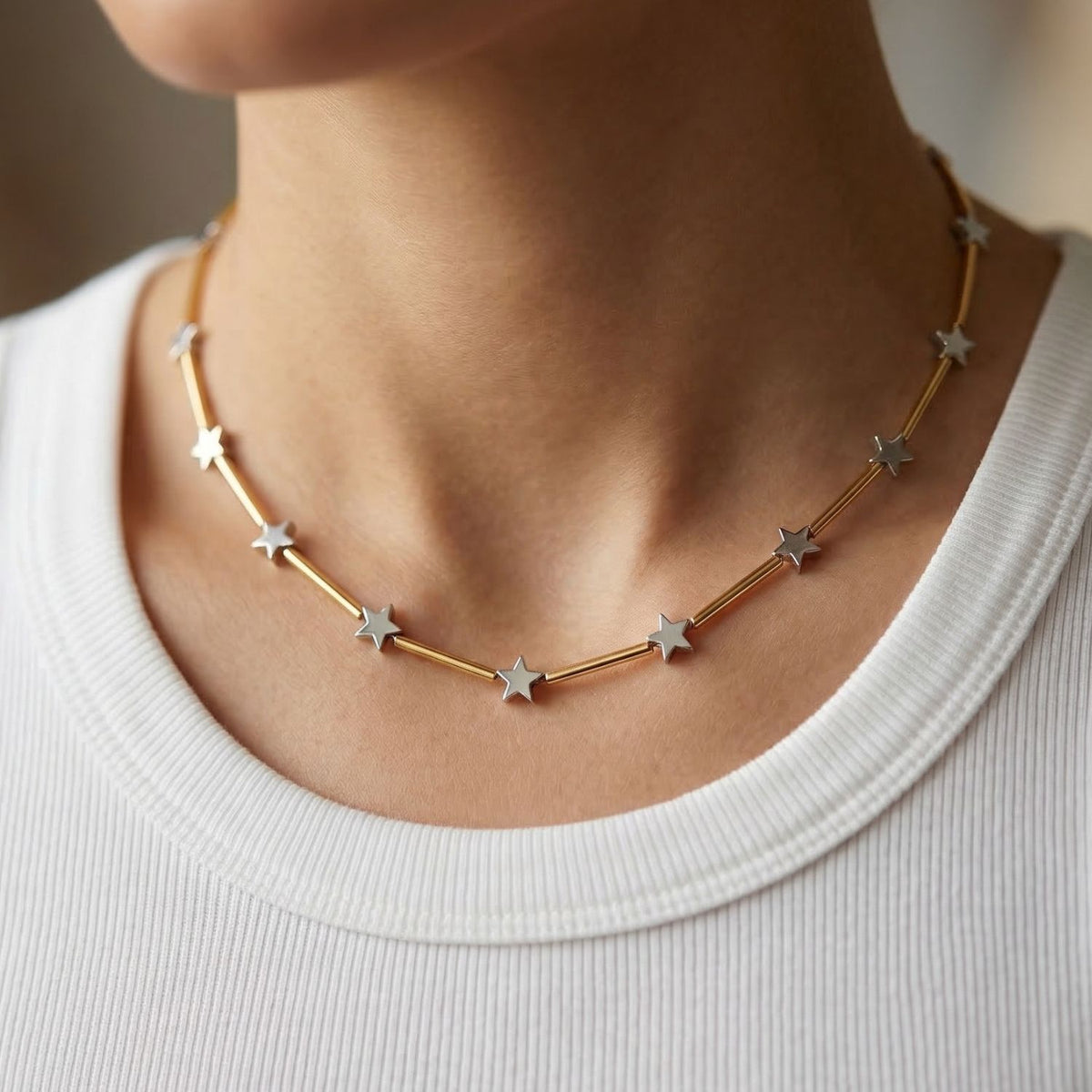 The Starlight Plated Hematite Necklace—a gold-plated choker with brushed finish and silver star charms—crafted by JAREDJAMIN in West Hollywood: artisanal, sustainable, and textured for luxury. Shown atop a white ribbed shirt.