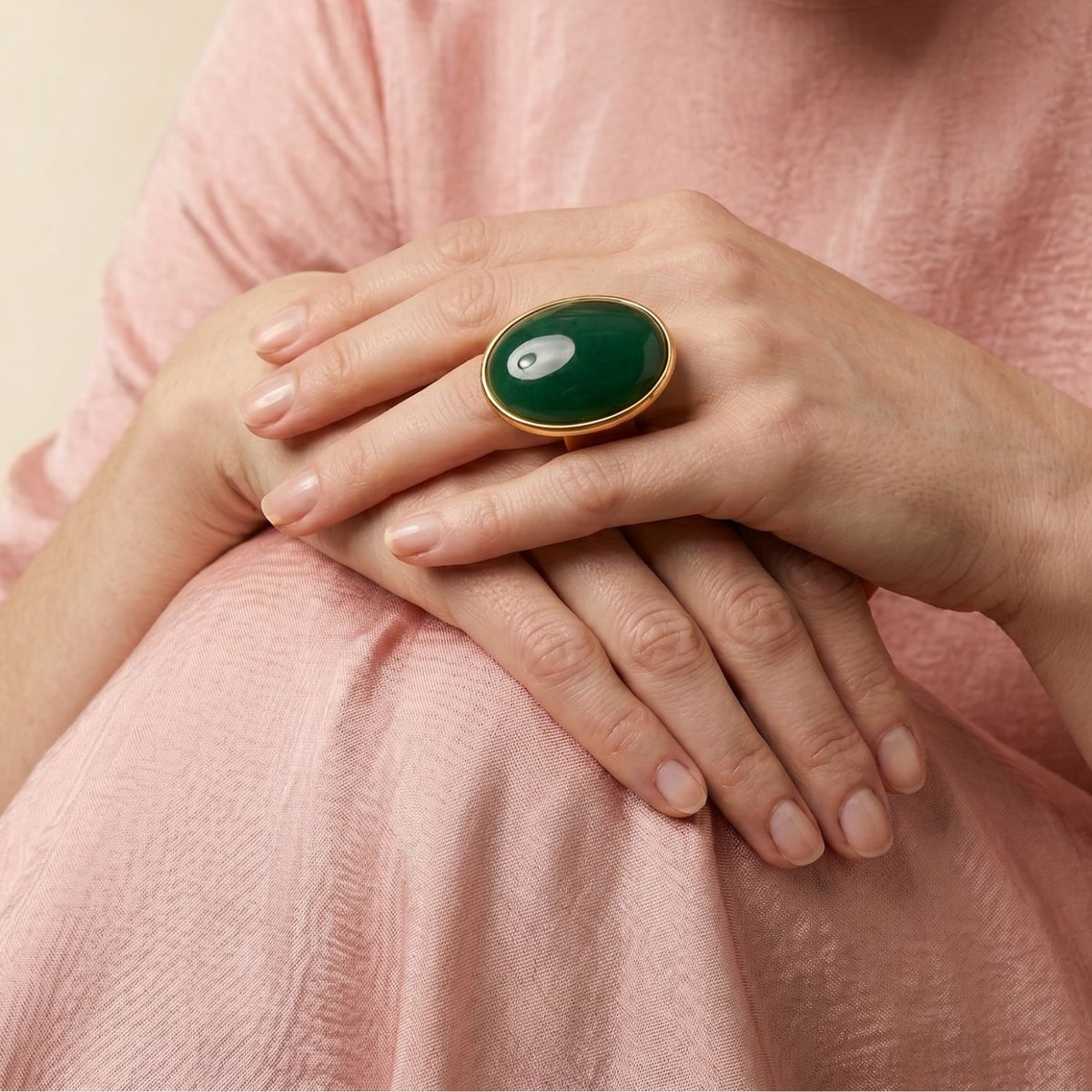Hands rest deliberately atop a pink textured dress, drawing focus to the hand-assembled Stella Statement Ring: Malaysia Jade centered on an 18k gold-plated band. Crafted in our West Hollywood studio using small-batch, eco-conscious methods. Style Note: punctuates everything from pared-back tailoring to silk slip dresses.