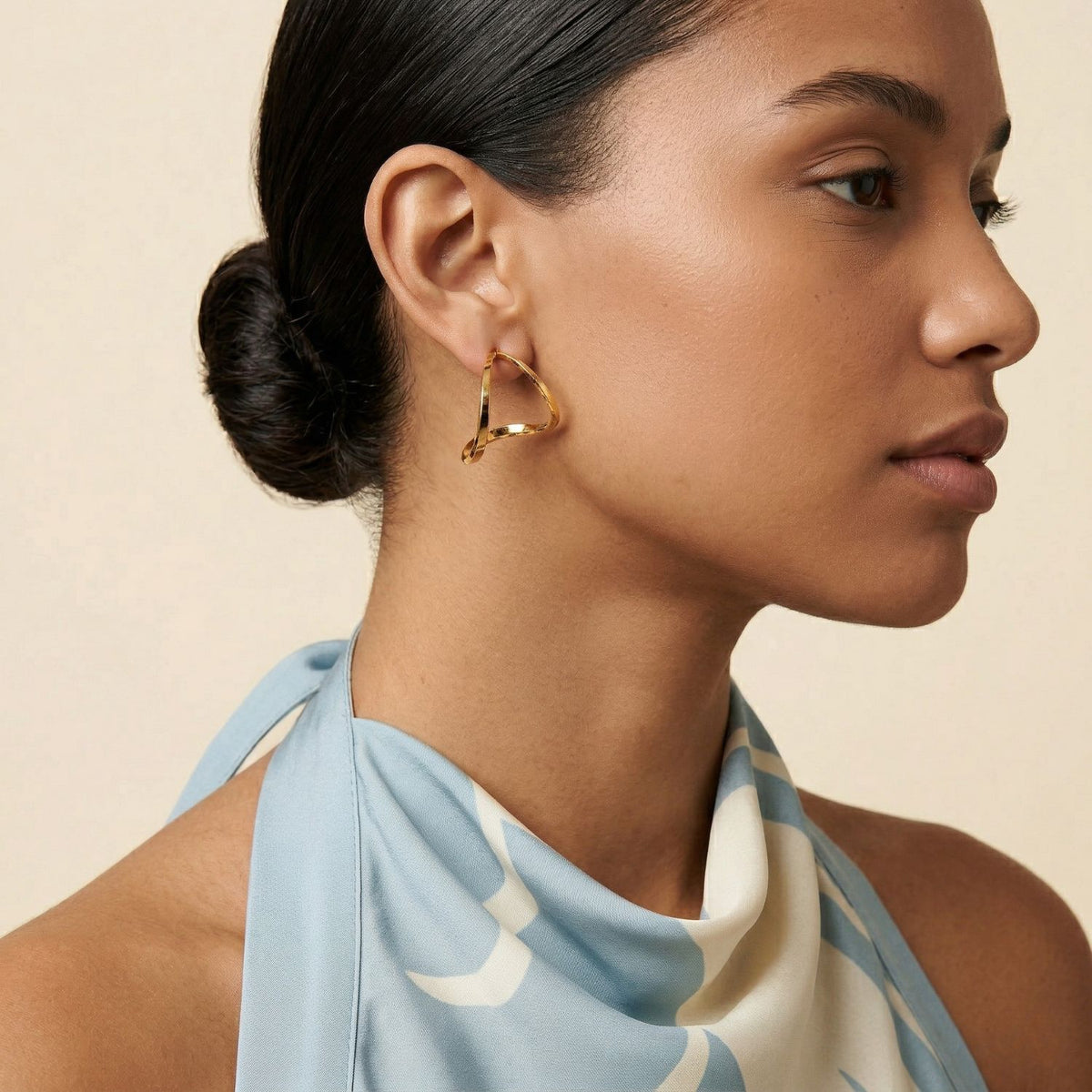 A woman with luminous skin and dark hair swept into a low bun showcases the Tabby Earrings—twisted 18k gold plate double hoops, hand-assembled in our West Hollywood studio. Crafted in small batches with eco-minded intent. Style note: punctuates soft knits or sharp tailoring.