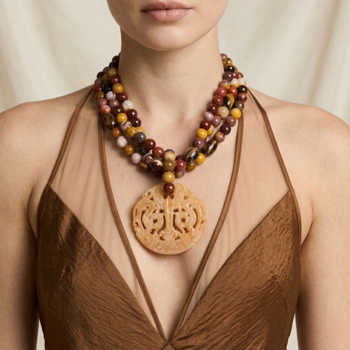 Model wearing the Jared Jamin Temple Pass Necklace, showing the three-strand Jasper beads and carved stone pendant resting at an 18-inch length. The shot demonstrates the tiered drape and natural stone texture against the skin.