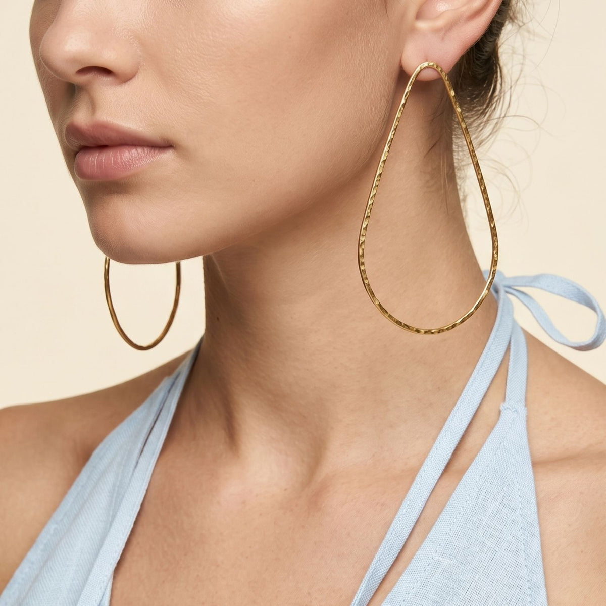 Side profile portrait view of a model wearing the 4-inch Tereza Single Teardrop Post Earrings, demonstrating their airy, open floating silhouette and light-catching gold surface styled with a light blue halter top.