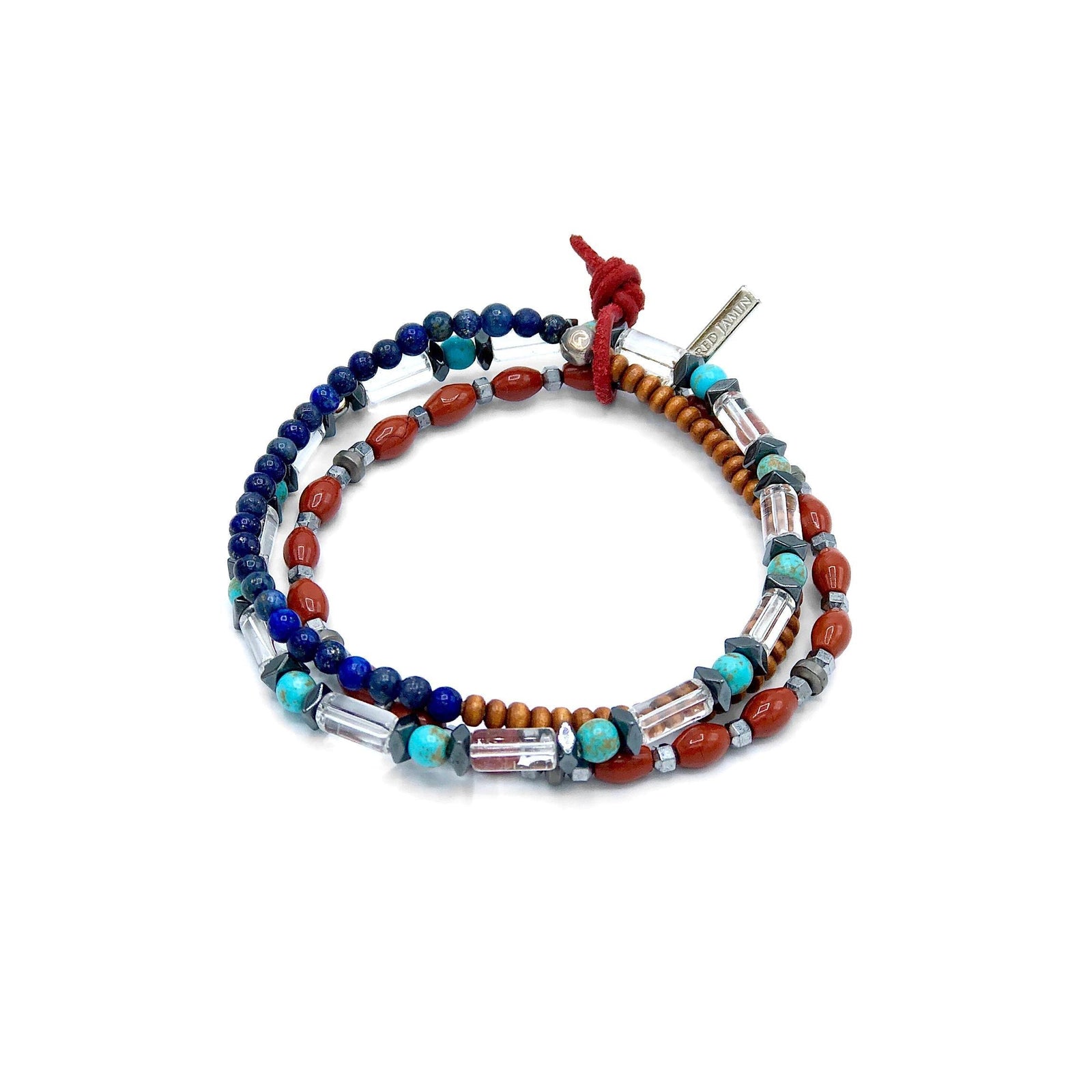 The Dwayne Bracelet Set by JAREDJAMIN Jewelry Online features multicolored strands of red, blue, turquoise, wood-toned, and clear beads with jasper accents, silver beads, a red cord knot closure, and a metallic tag in a coiled circle design.