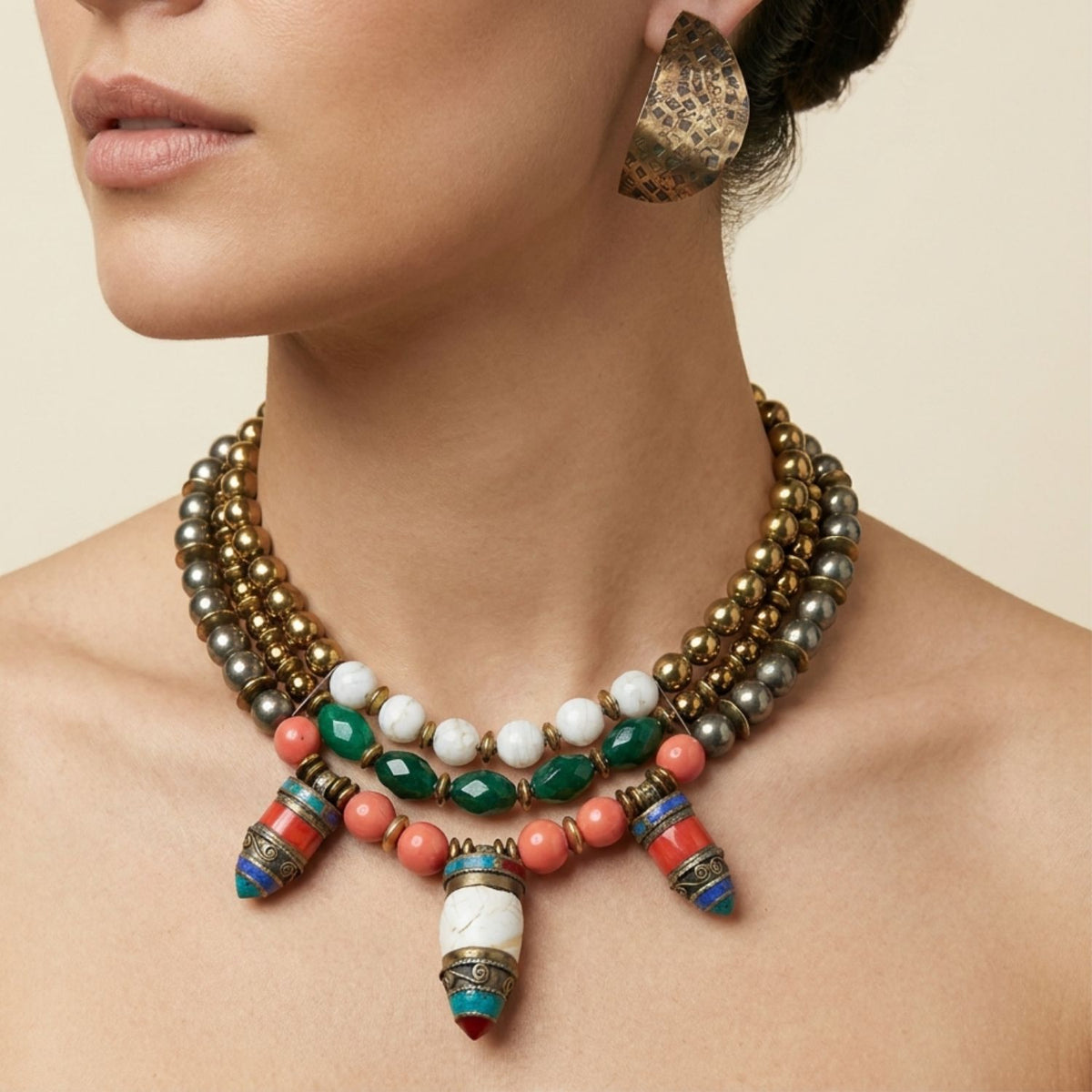 Close-up profile portrait of a model wearing the JAREDJAMIN Tibetan Tide One-of-a-Kind Multi-Strand Collar Necklace against a neutral background, highlighting its multi-tiered metal beads, green agate, coral-colored beads, and central inlaid amulet pendants.