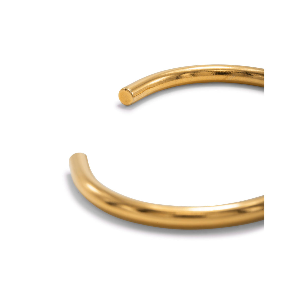 gros plan of the JAREDJAMIN Bijoux en Ligne or Tubular manchette, an élégant, or-colored, open-ended bracelet avec a smooth, poli surface et simple rounded design against a fond blanc. Only part of the manchette is visible.