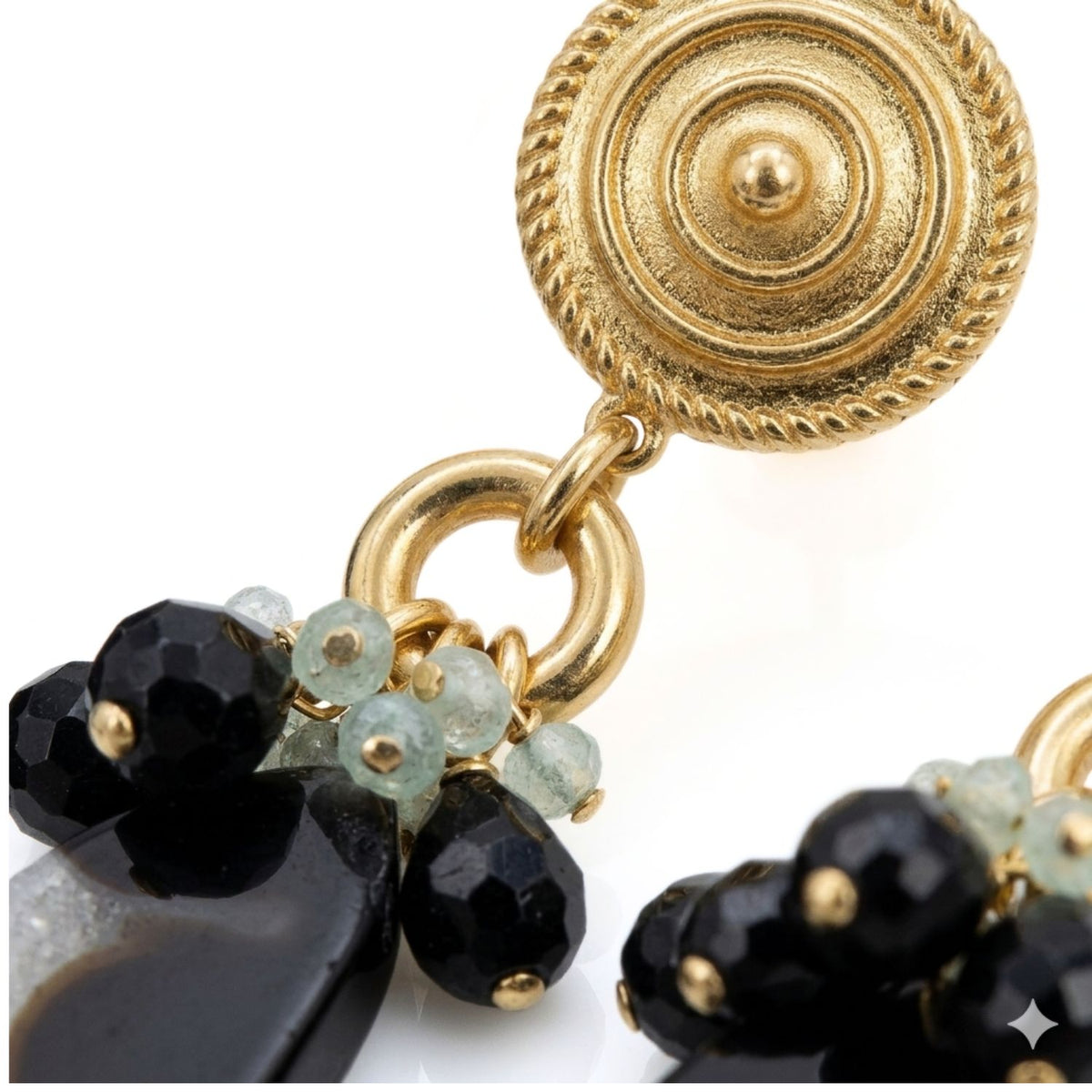 Close-up studio macro shot focusing on the textured golden shield clip-on top, circular connecting ring, dark faceted crystal beads, and small pale green crystal accents.