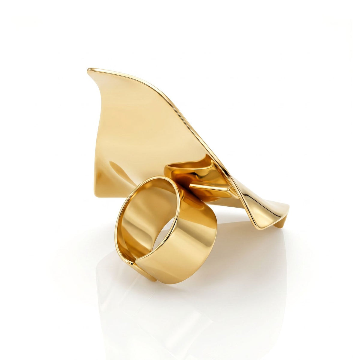 Side angle studio shot of the gold sculptural wave ring resting on a reflective surface, showcasing the thick, smooth adjustable band hidden beneath the curved, wave-like architectural metal plate.