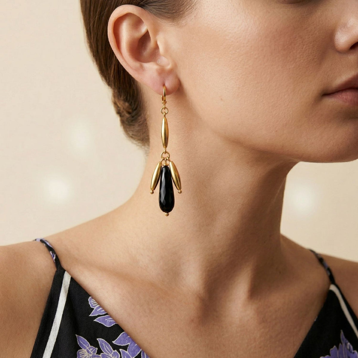 A woman with light skin and tied-back hair wears hand-assembled Wisteria Dangle Leverback Earrings: elongated onyx drops punctuated by gold-tone beads, crafted in our West Hollywood studio. Small-batch, eco-conscious. Style Note: transitions from sharp tailoring to evening silk.