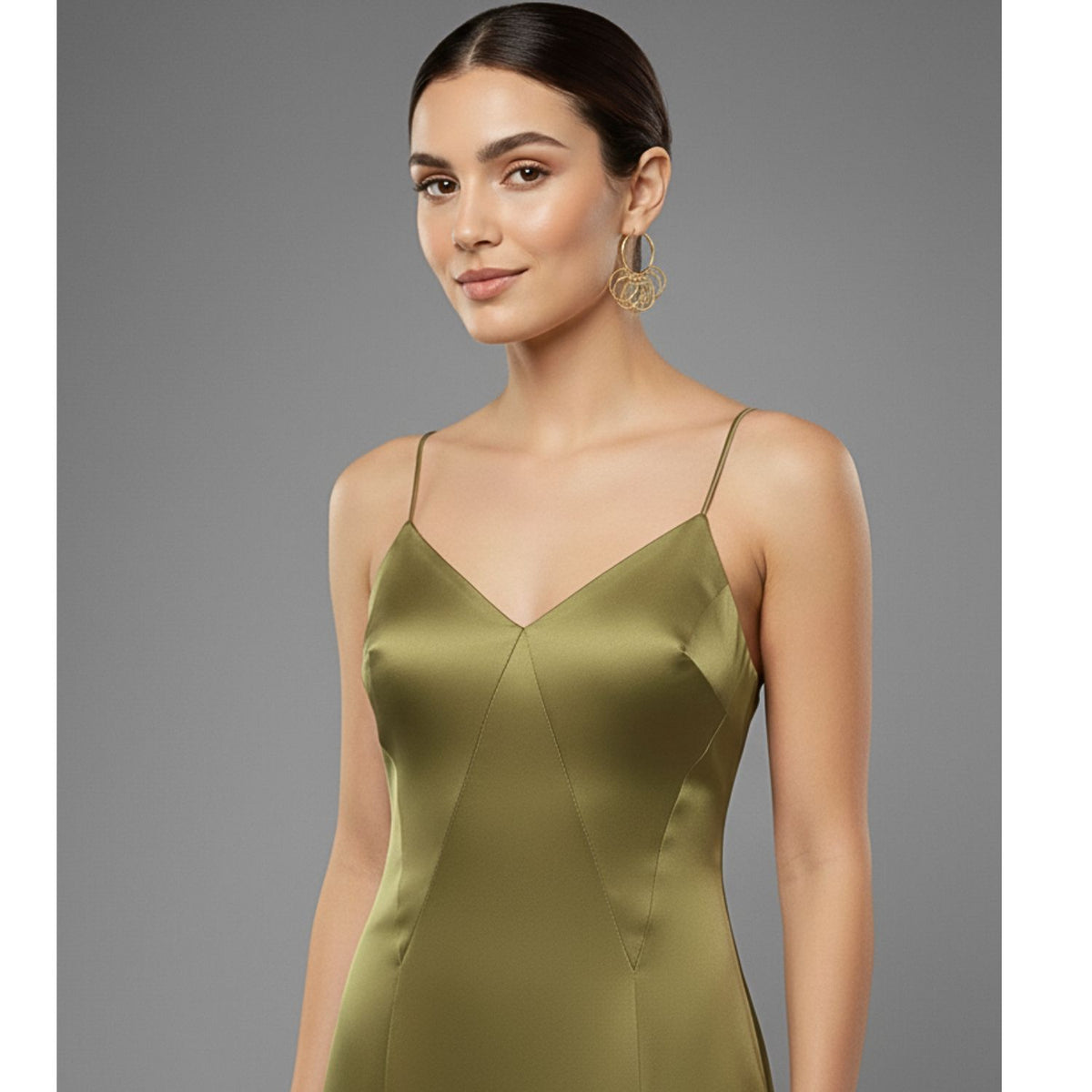 A woman with dark hair in a sleek low bun wears JAREDJAMIN Jewelry Online’s Zephyr Hoop Click-Top Earrings. She pairs them with a shiny olive-green spaghetti strap dress and poses softly against a plain gray background.
