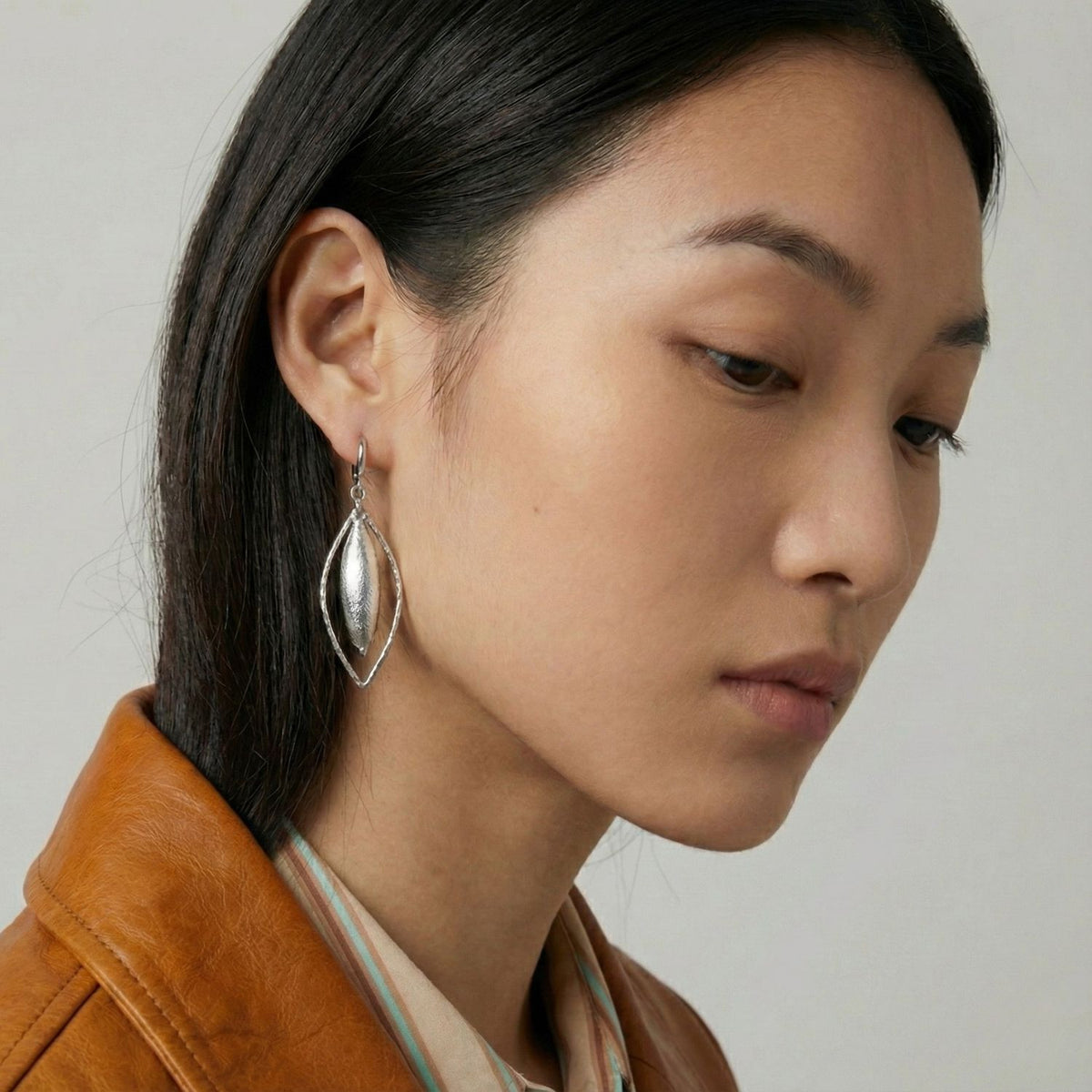 Zeppelin Haley plata Leverback pendientes Small de JAREDJAMIN joyería showcase sustainable de lujo in brushed sterling plata, artisanally crafted in small batches in West Hollywood. Signature texture gleams against a light backdrop y brown leather jacket.