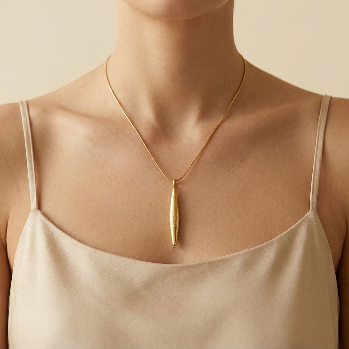 A woman in a beige camisole punctuates her look with the Large Gold Zeppelin Pendant, its sculptural form hand-assembled in our West Hollywood studio. Each eco-conscious, small-batch piece refracts light—style note: effortless from tailored suiting to slip dresses.