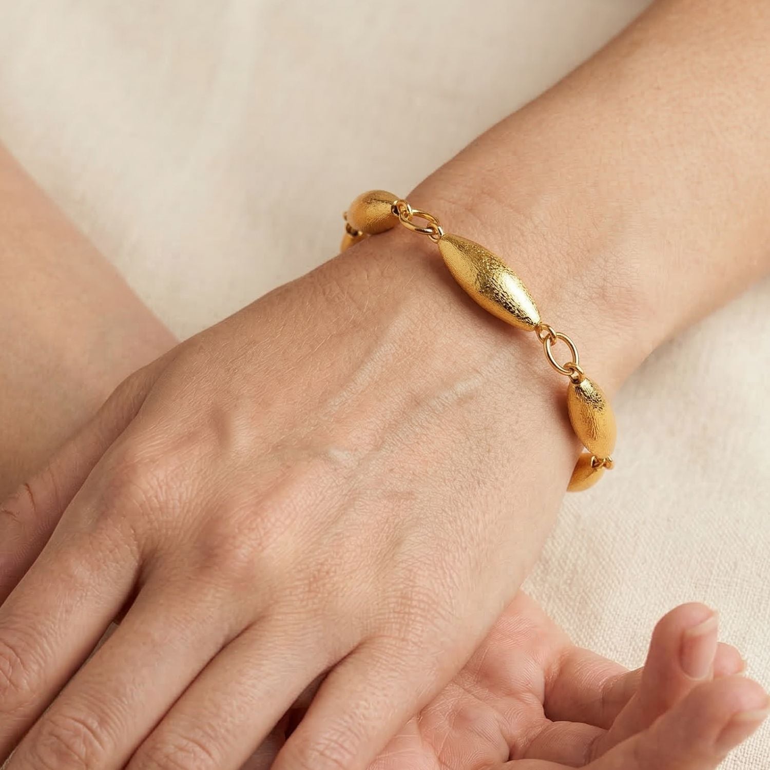 The Zeppelin Phoebe Gold Bracelet by JAREDJAMIN Jewelry Online showcases four linked, textured oval beads and a sleek toggle clasp. Crafted with an 18K gold-plated finish, it is elegantly symmetrical and includes a small tag detail.