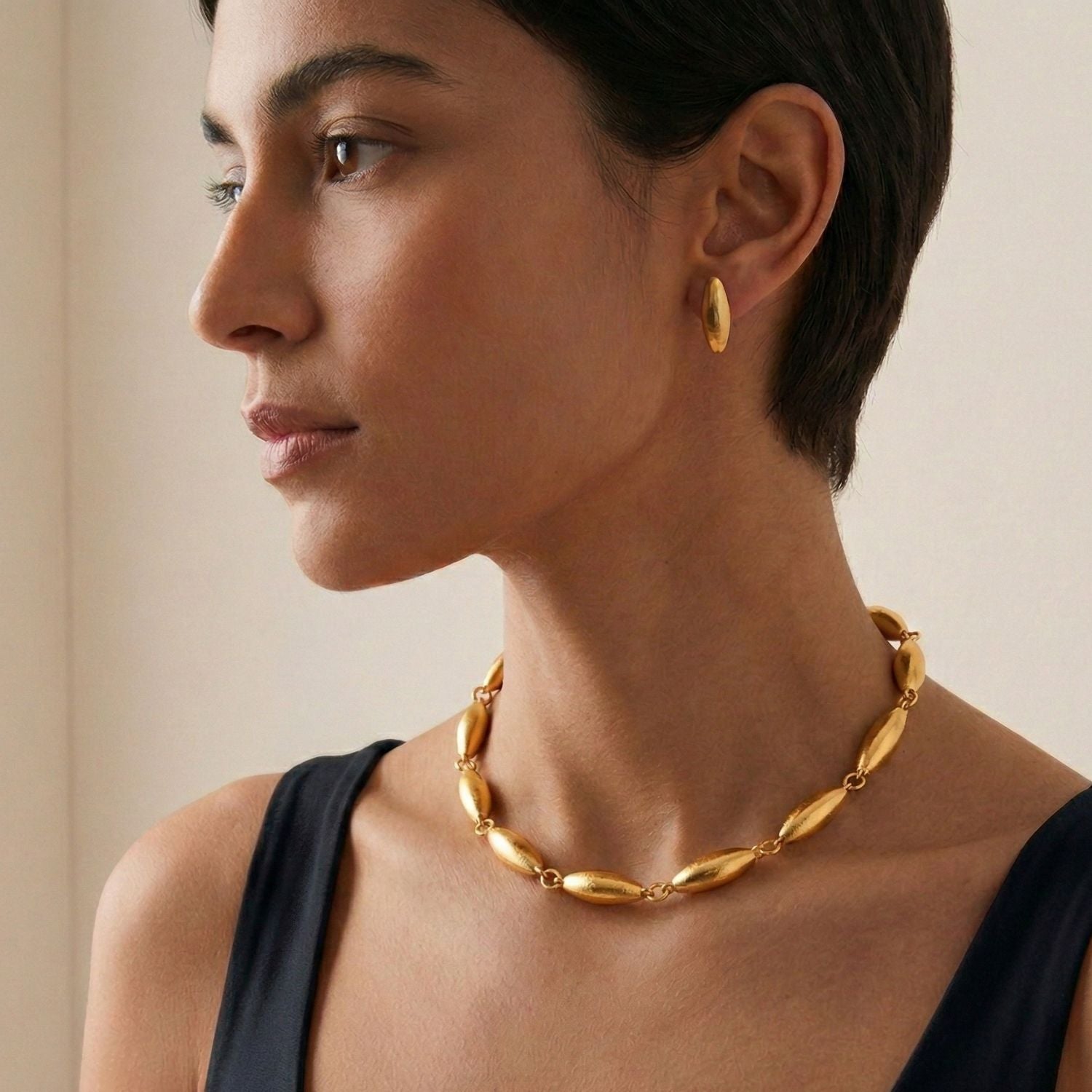 The Zeppelin Gold Stud Post Earrings from JAREDJAMIN Jewelry Online feature 18K goldplating, an oval domed shape, and a brush-textured matte finish. Shown diagonally on a white background with soft shadows.