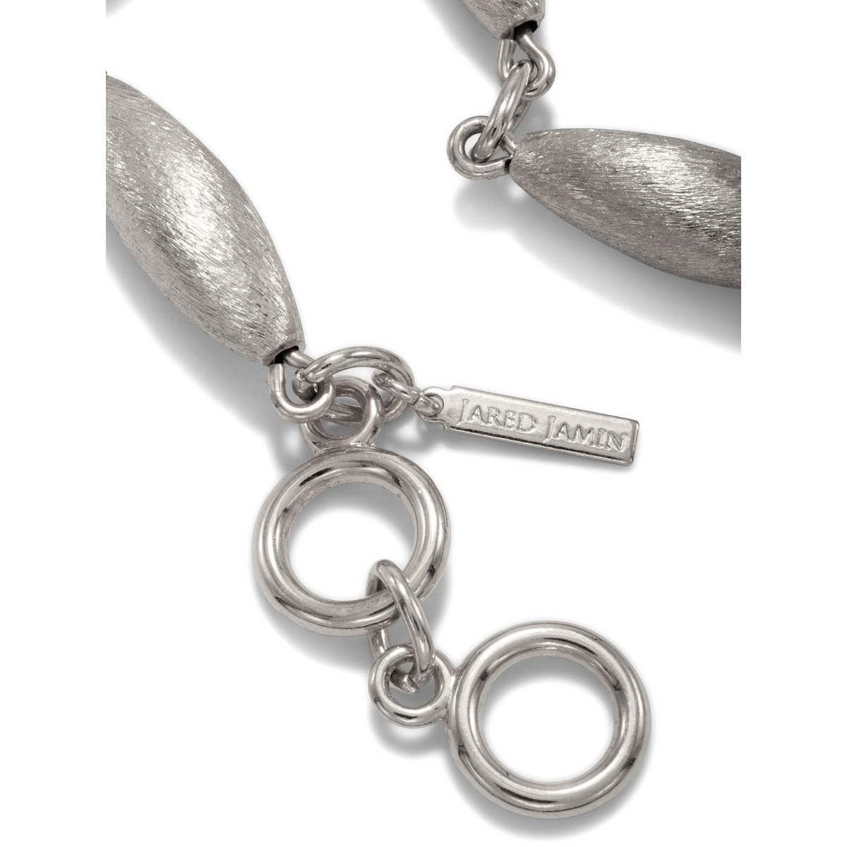 Un primer plano of the Zeppelin Phoebe plata collar de JAREDJAMIN Joyería Online shows texturizado oval y smooth circular links con a plata-plated clasp, plus a tag engraved "JARED JAMIN," all set against a plain fondo blanco.