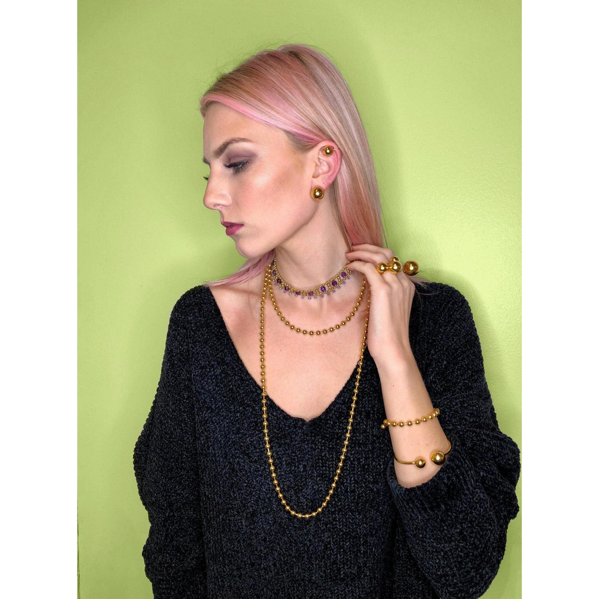 Un woman avec pale skin et pink hair dans un black sweater poses against a light green background, wearing the or Orbita Ear manchette boucle d'oreille par JAREDJAMIN Bijoux en Ligne pour un audacieux, modern, unisex look. She gazes to the side neutrally.