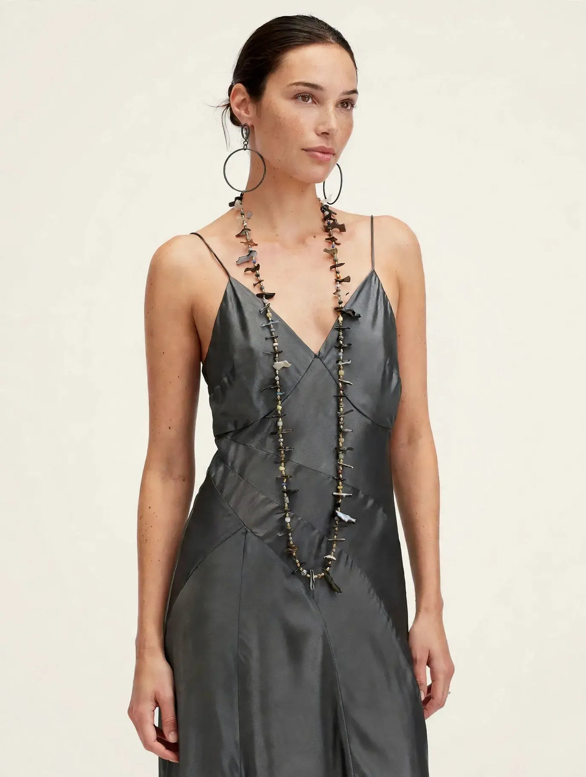 Caracola shell shard necklace styled long on a model in a charcoal silk dress with Ophelia earrings