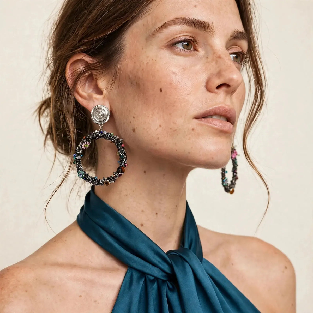 Close model view of Simone clip-on earrings — silver disc clip-ons with dark crocheted multicolor crystal hoops — teal satin halter top