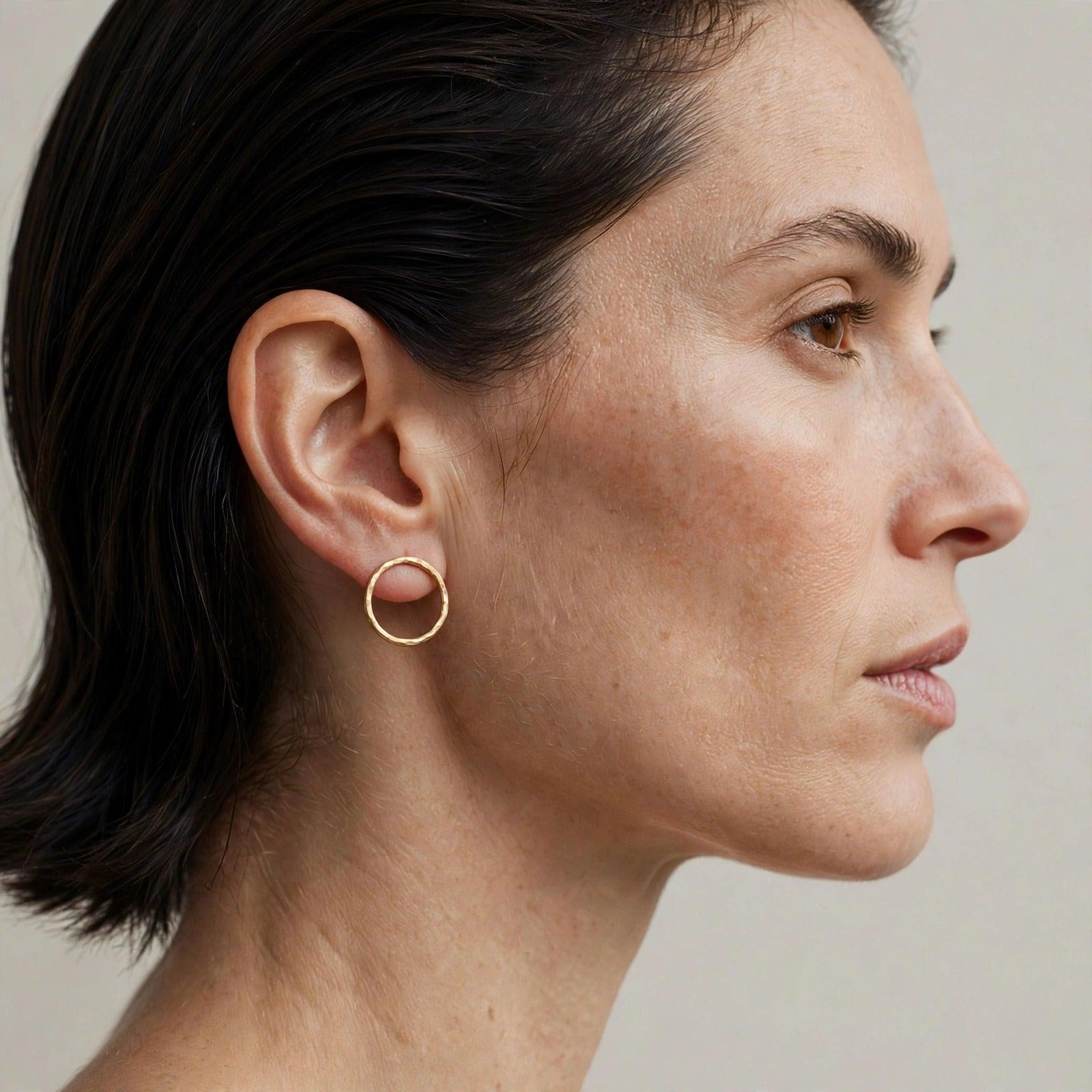 Medium Rhodri Textured Circular Post Earrings in 18k gold plate — a pair of hand-hammered closed gold rings, one inch in diameter, on a white background.
