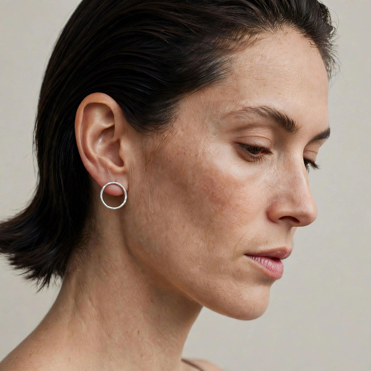Model wearing the Medium Rhodri Textured Circular Post Earrings in silver plate — a one-inch hand-hammered closed silver ring stud on the earlobe.