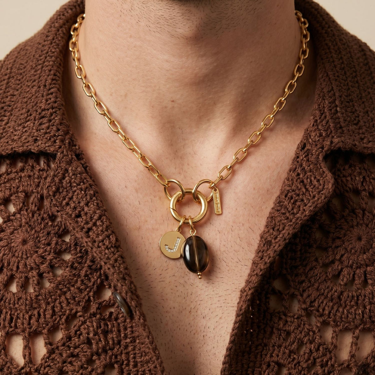 A close-up frames a neck adorned with our hand-assembled Smoky Quartz Pebble Pendant, gold “J” disc, and signature tag—meticulously crafted in West Hollywood using small-batch, eco-conscious methods. Style Note: punctuates knits, silks, or tailoring.