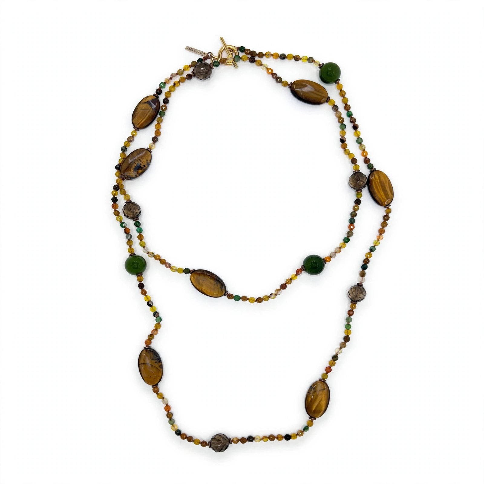 A long beaded necklace arranged in a vertical S-curve on a white background: oval tiger's eye cabochons with golden-brown bands, dark faceted smoky quartz rounds, and green gemstone rounds spaced along the strand, each separated by runs of tiny faceted agate beads in amber, honey, olive, and brown; a gold-tone toggle clasp and small JAREDJAMIN tag at the top.
