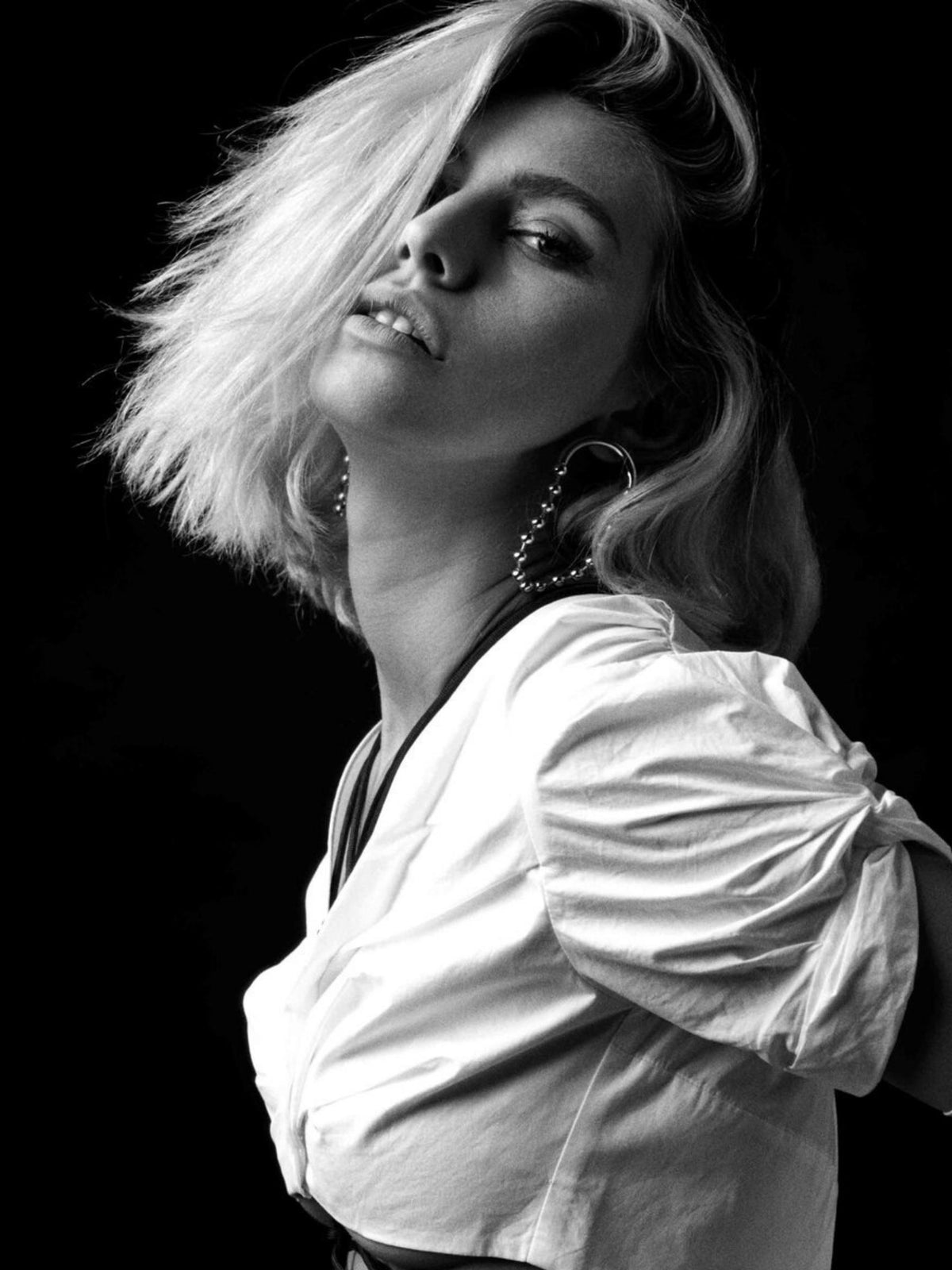 or Orbita Amari boucles d'oreilles de JAREDJAMIN Bijoux en Ligne are showcased by a woman posing against a black background dans un white, ruched-sleeve top. Her blonde, tousled hair partially covers her face as she looks neutrally at the camera.