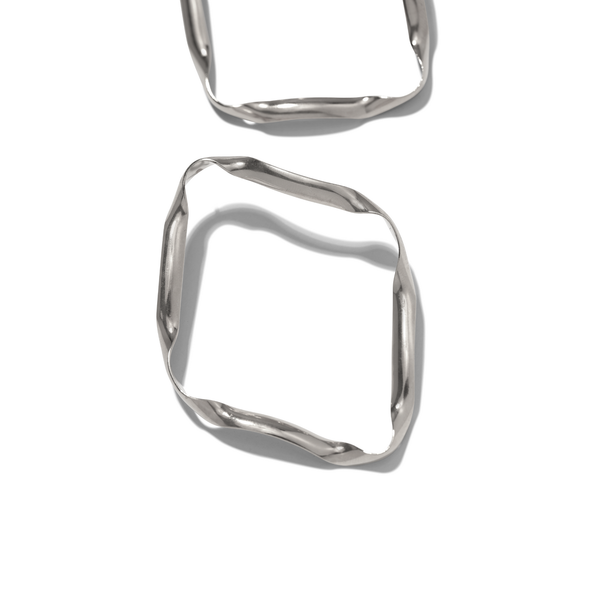 Two argent Ribbonelle boucles d'oreilles par JAREDJAMIN Bijoux en Ligne, avec irregular, wavy edges et a unique design, rest sur un fond blanc. One boucle d'oreille is fully visible at the bottom; the other is partially cropped at the top. Soft shadows appear below.